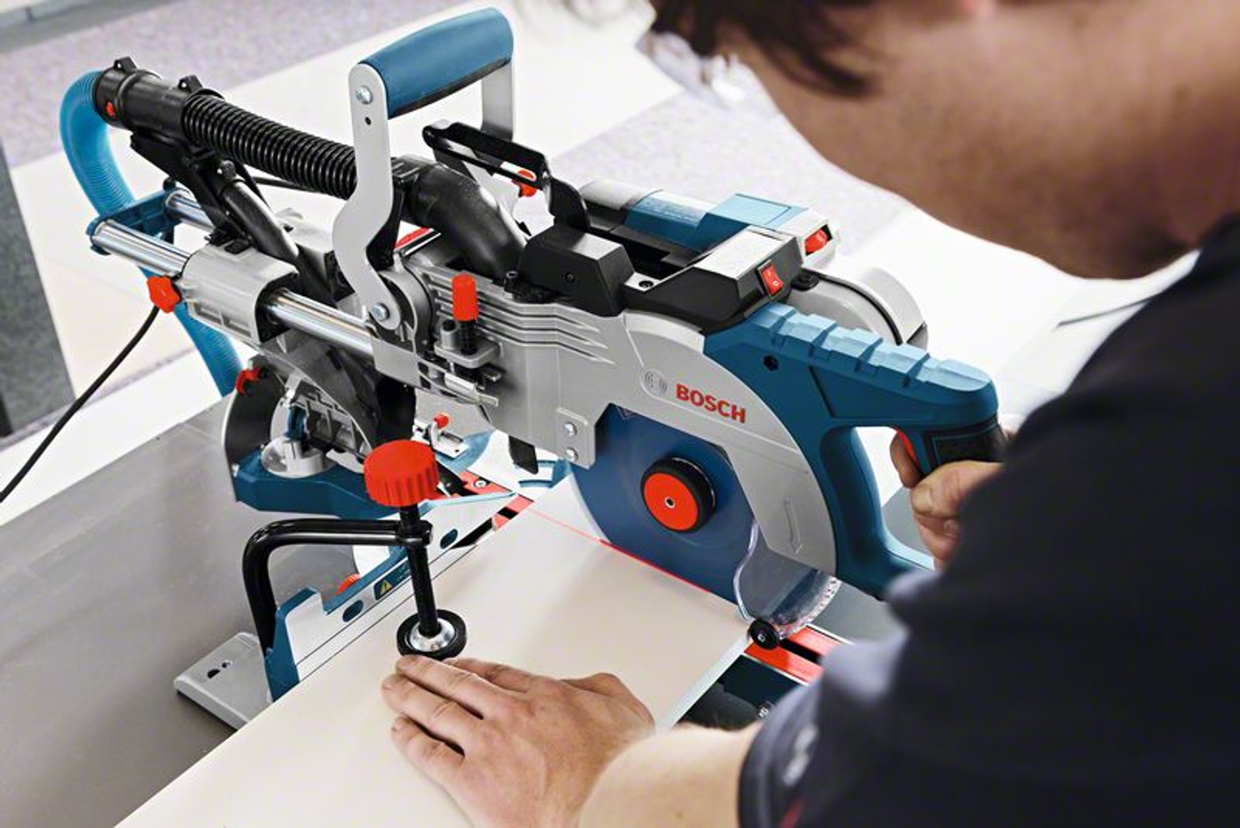 Una persona usando una sierra ingletadora Bosch, cortando un trozo de madera blanca.