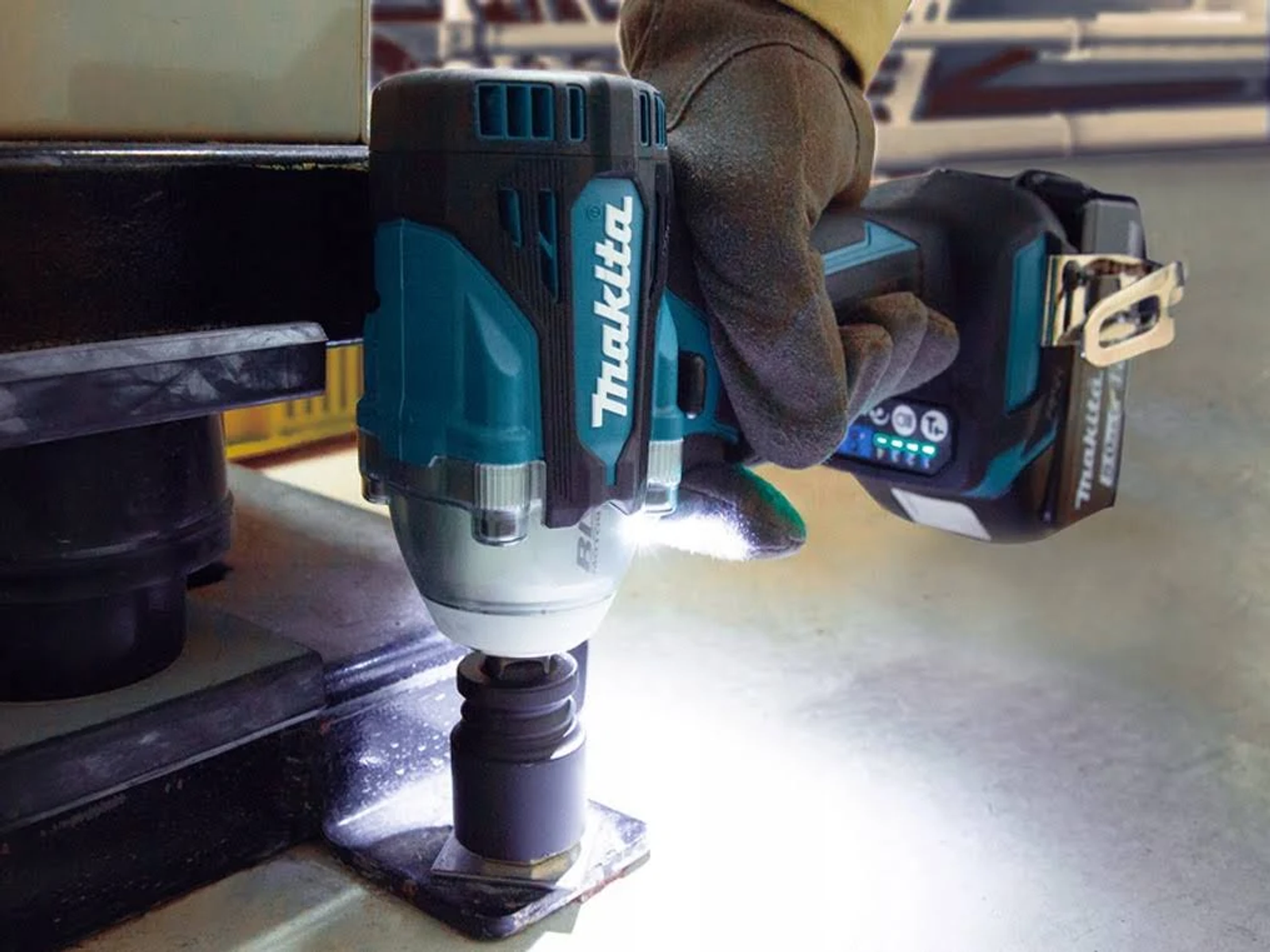Una persona usando una llave de impacto Makita verde azulado y negra. Fondo blanco.