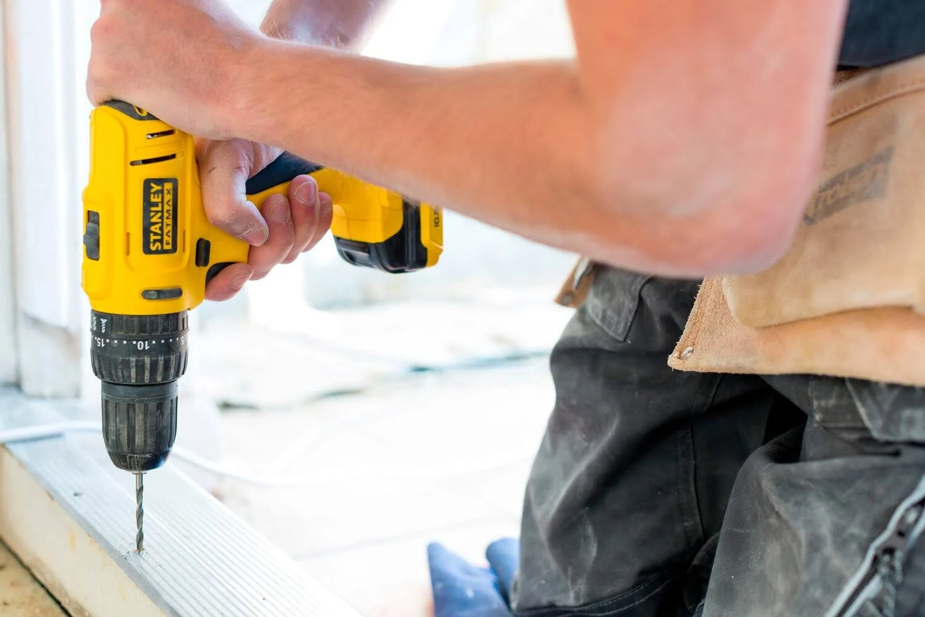 Persona taladrando en un marco de madera con un taladro Stanley Fatmax amarillo. Fondo claro.