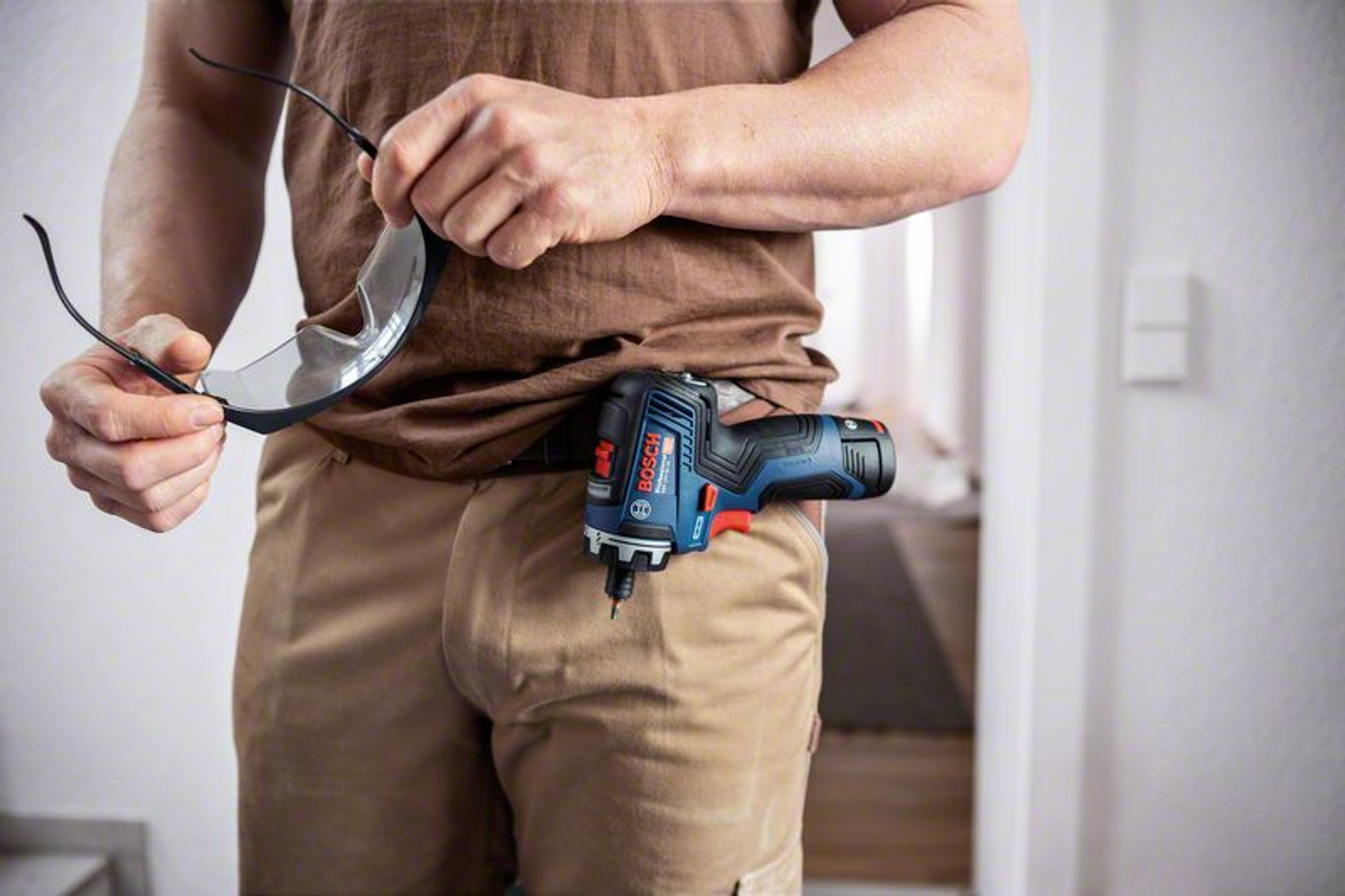 Mężczyzna trzyma okulary ochronne z wkrętarką udarową Bosch w kieszeni.