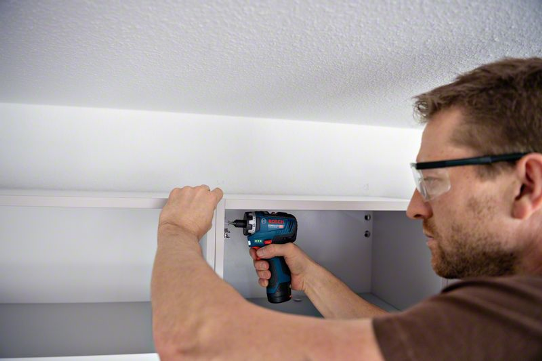 Mężczyzna używający niebiesko-czarnej wiertarki do wkręcania w szafkę.