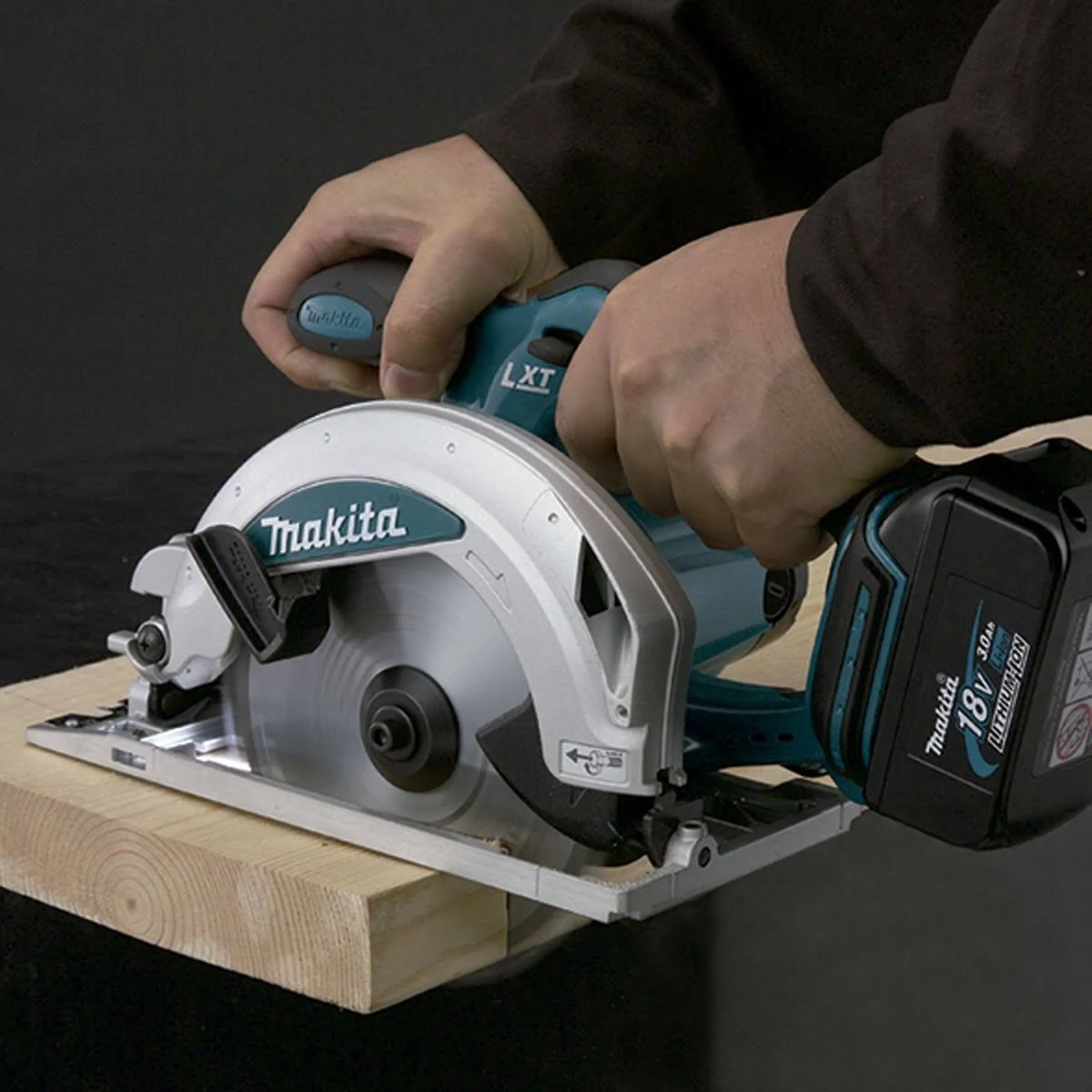 Una persona que usa una sierra circular Makita en una tabla de madera, fondo oscuro.
