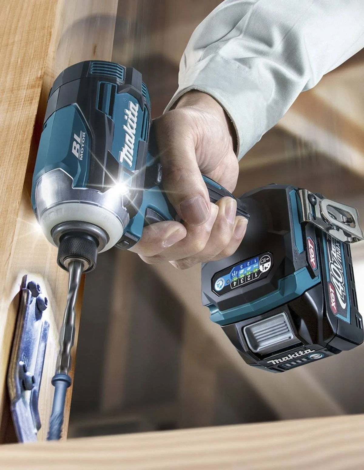 Una mano tiene un avvitatore a impulsi Makita, che avvita una vite nel legno. L'utensile è verde acqua e nero.