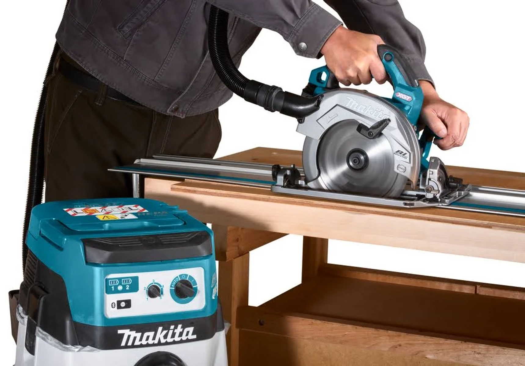 Mężczyzna używa piły szynowej Makita do cięcia drewna na drewnianym stole. Odkurzacz jest w pobliżu.