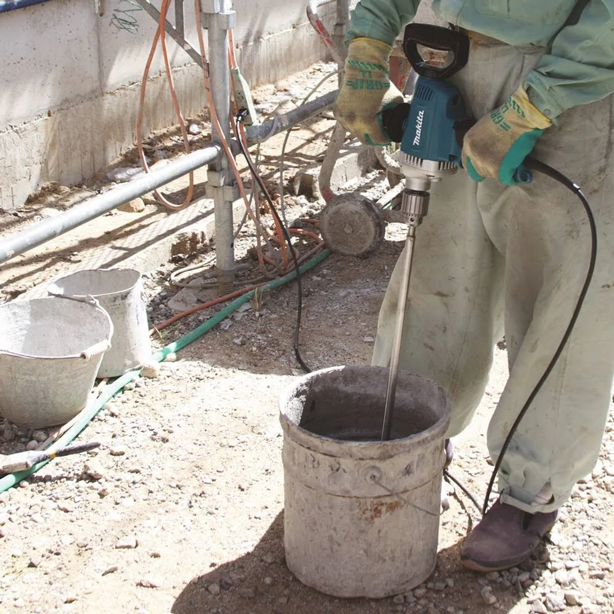 Una persona mescola cemento in un secchio con un miscelatore Makita. Secchi e attrezzi sono su cemento.