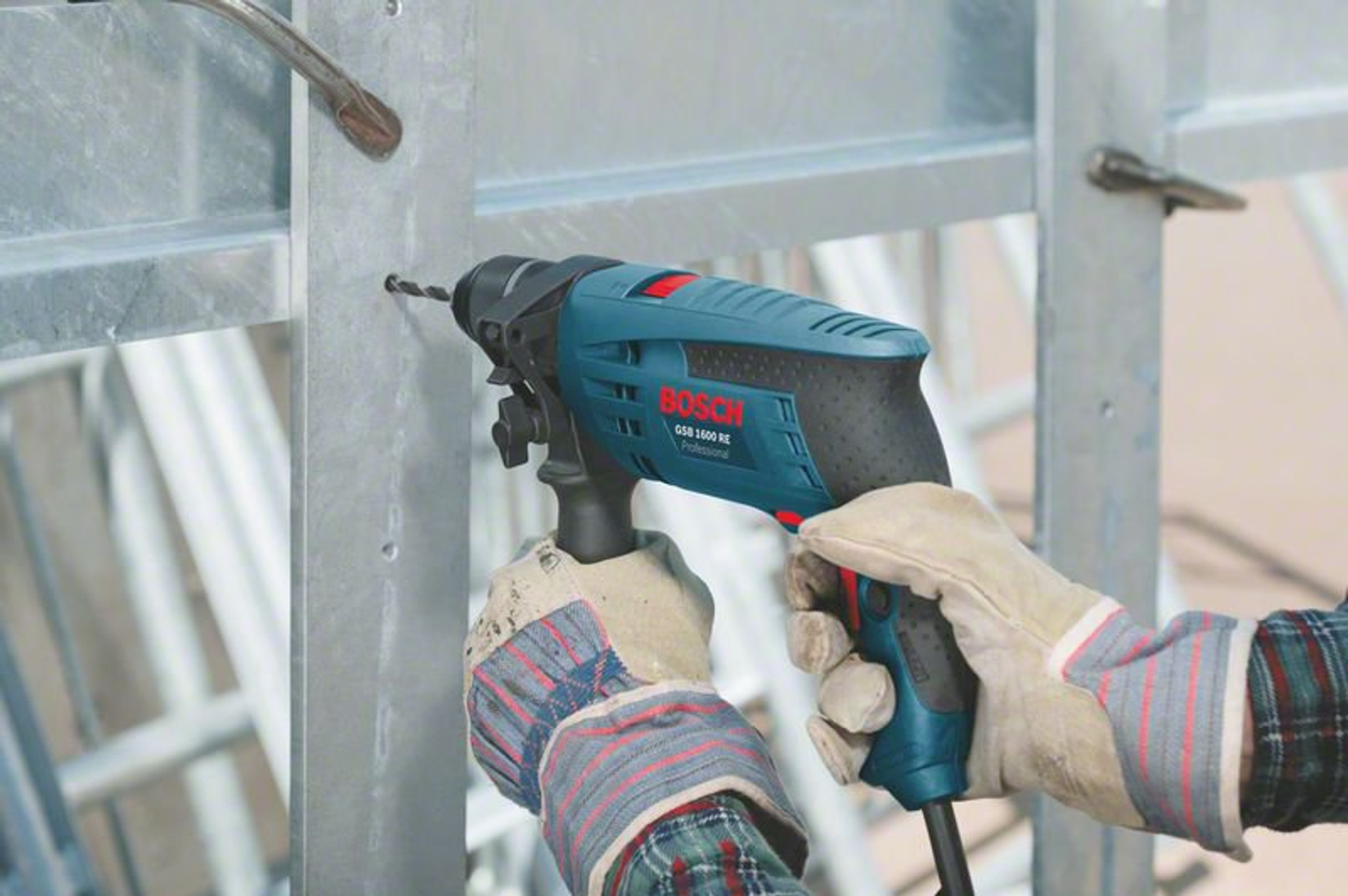 Una persona con i guanti sta forando un telaio metallico con un trapano Bosch. Lo sfondo è un cantiere.