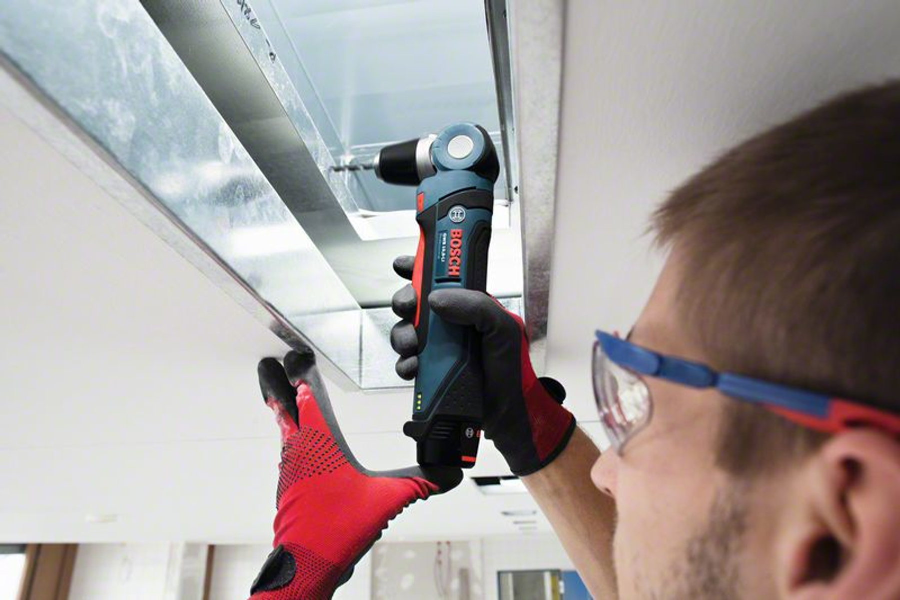 Mężczyzna wiercący w metalowej belce wiertłem w kolorze morskim i czarnym.