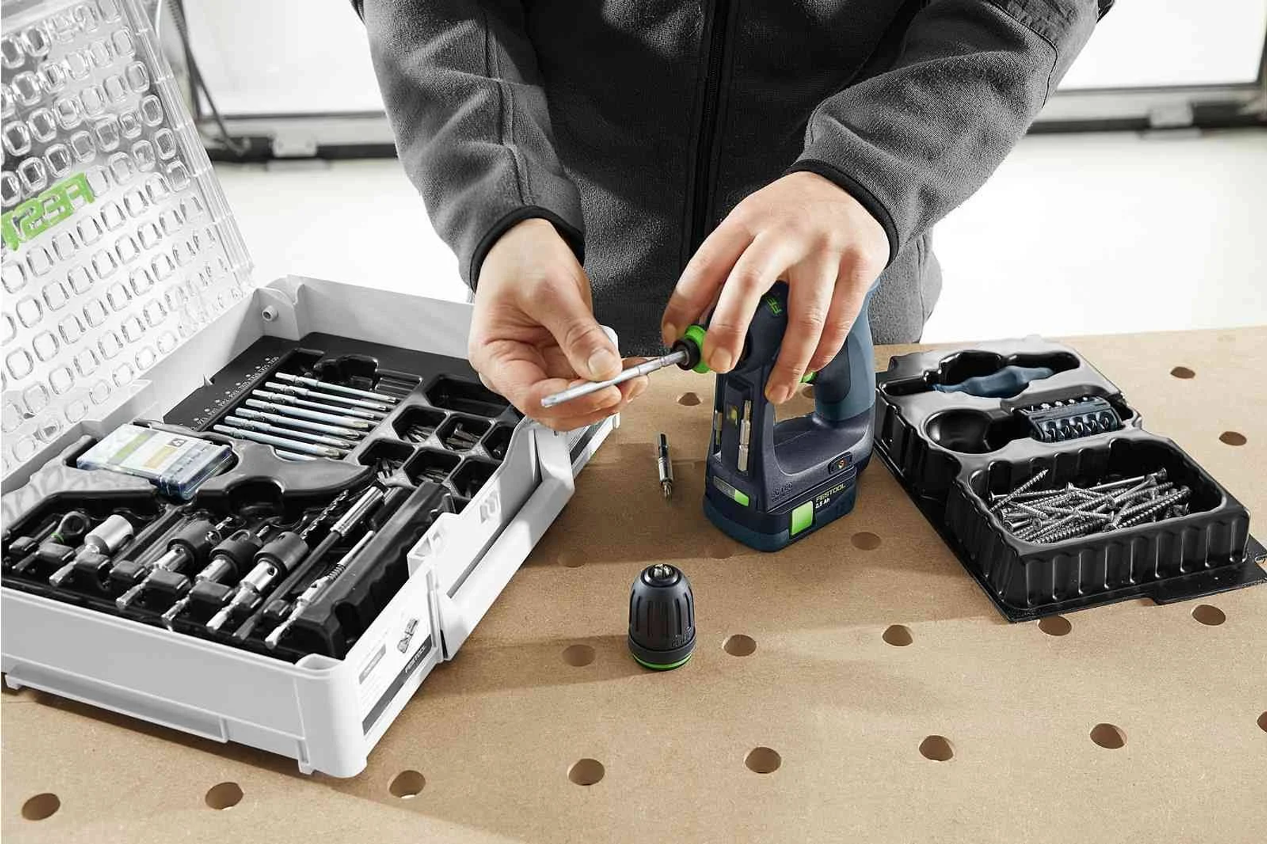 Una persona ensamblando un taladro con accesorios sobre una superficie de madera. Herramientas visibles.