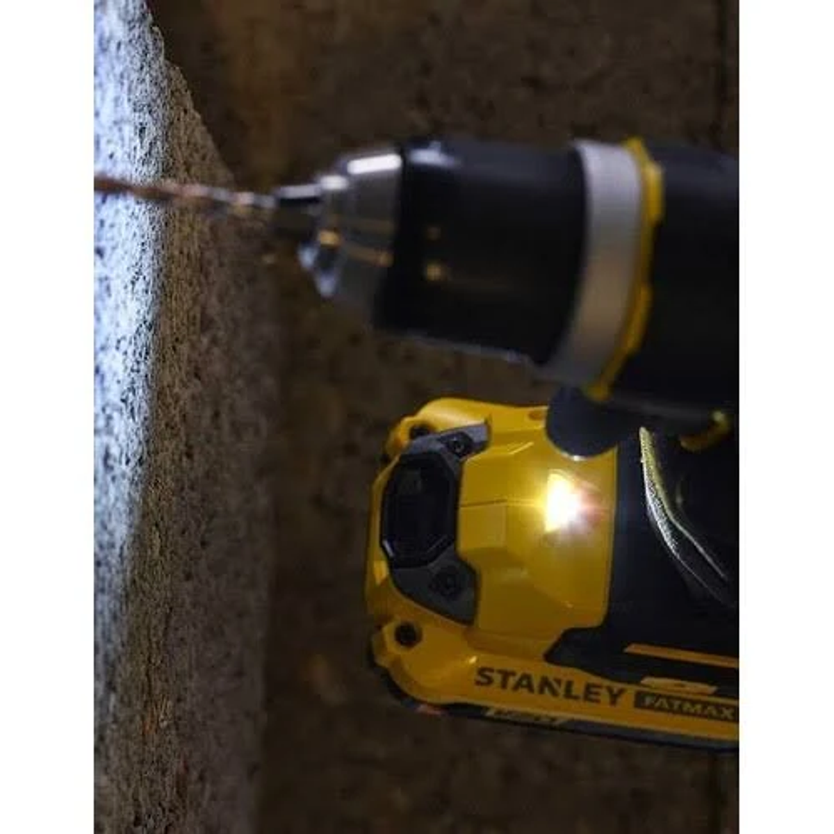 Un taladro amarillo Stanley Fatmax con luz encendida, perforando una pared gris.