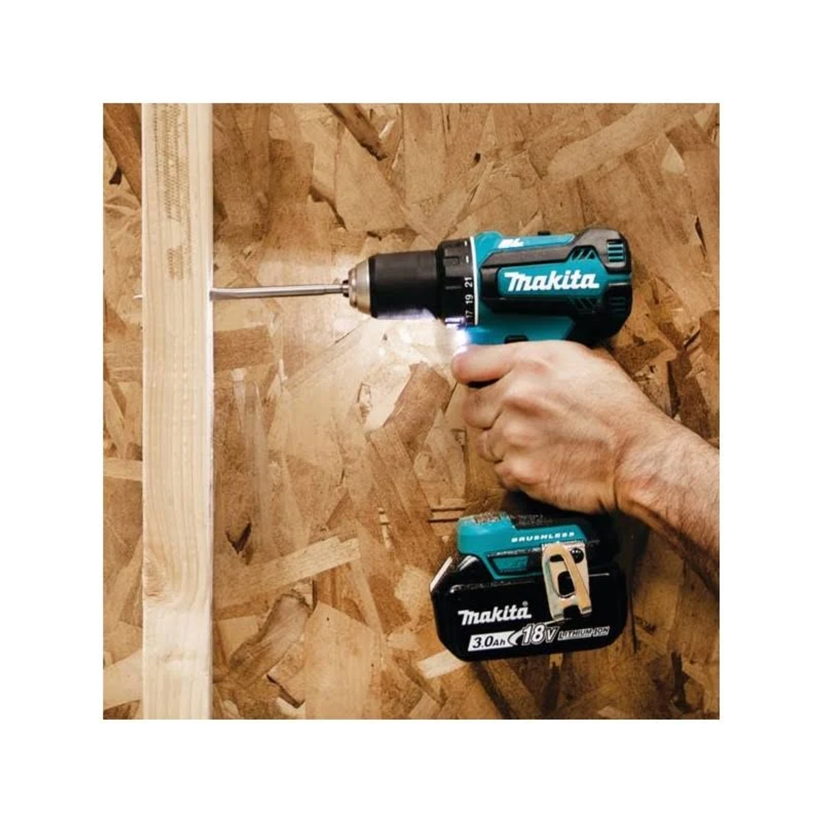 Eine Hand bohrt mit einer Makita-Bohrmaschine in Holz. Die Bohrmaschine ist türkisblau und schwarz und hat einen Akku.