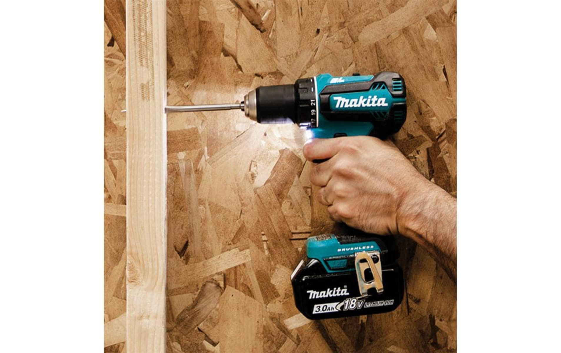 Eine Hand, die einen schwarzen und teal farbenen Bohrer hält, der in eine Holztafel bohrt.