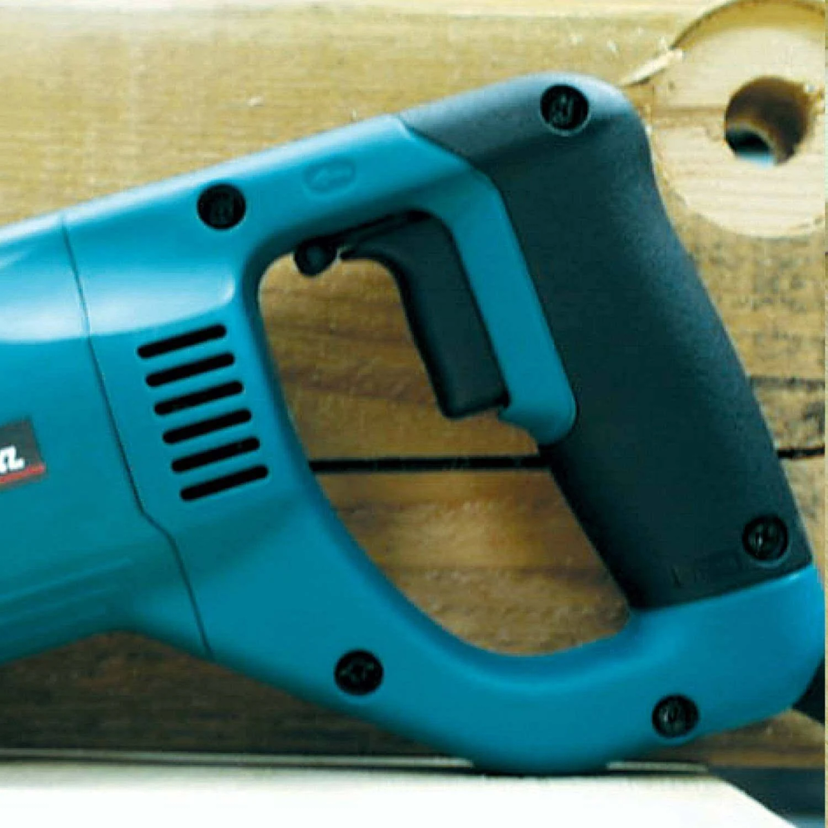 Zbliżenie na turkusowo-czarną piłę szablastą. Jest zamontowana na drewnianej powierzchni.