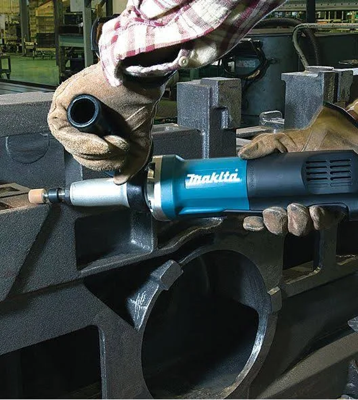 Manos usando herramienta Makita en superficie metálica. Herramienta turquesa, guantes grises.