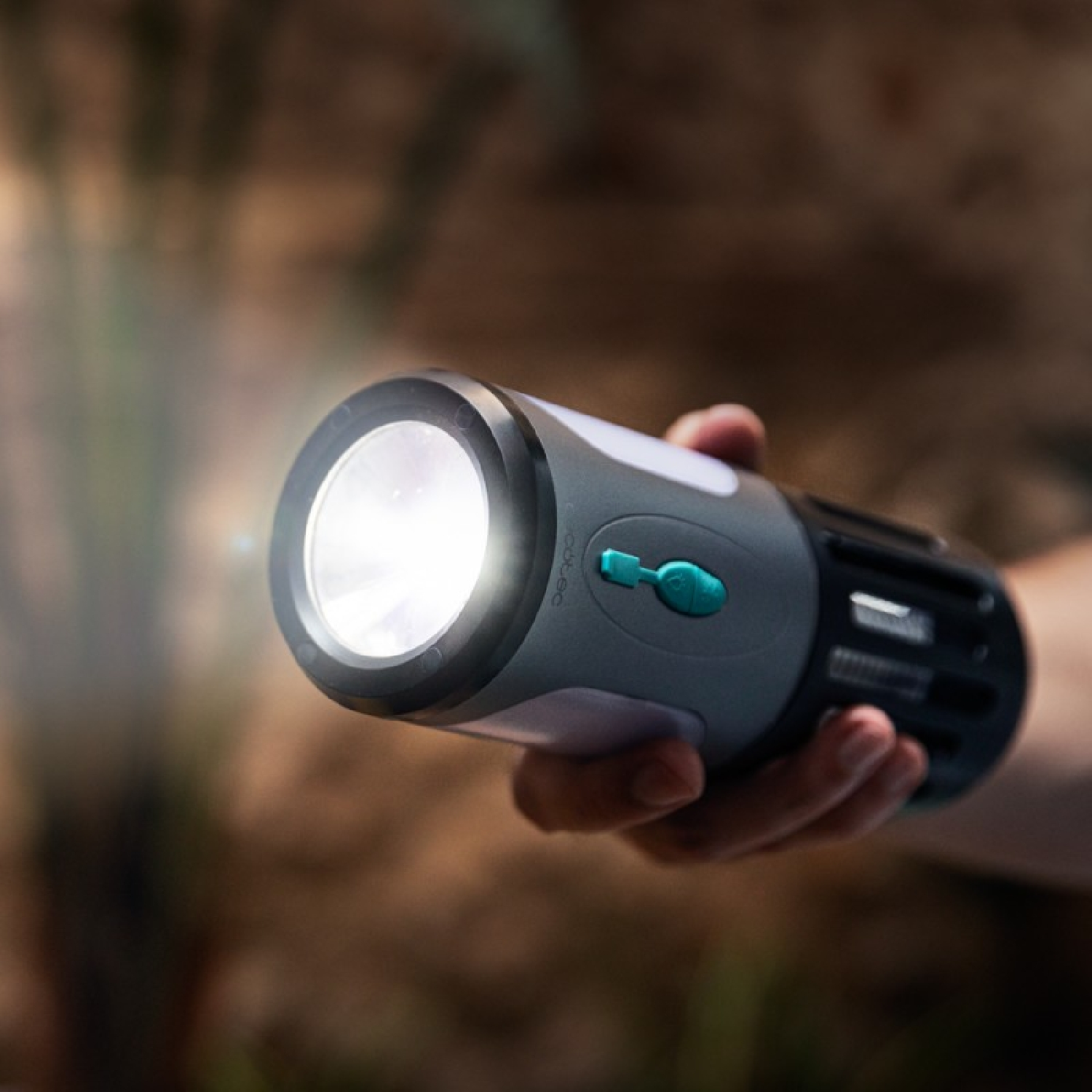 Eine Hand hält eine schwarz-graue Taschenlampe mit hellem Licht im Freien.