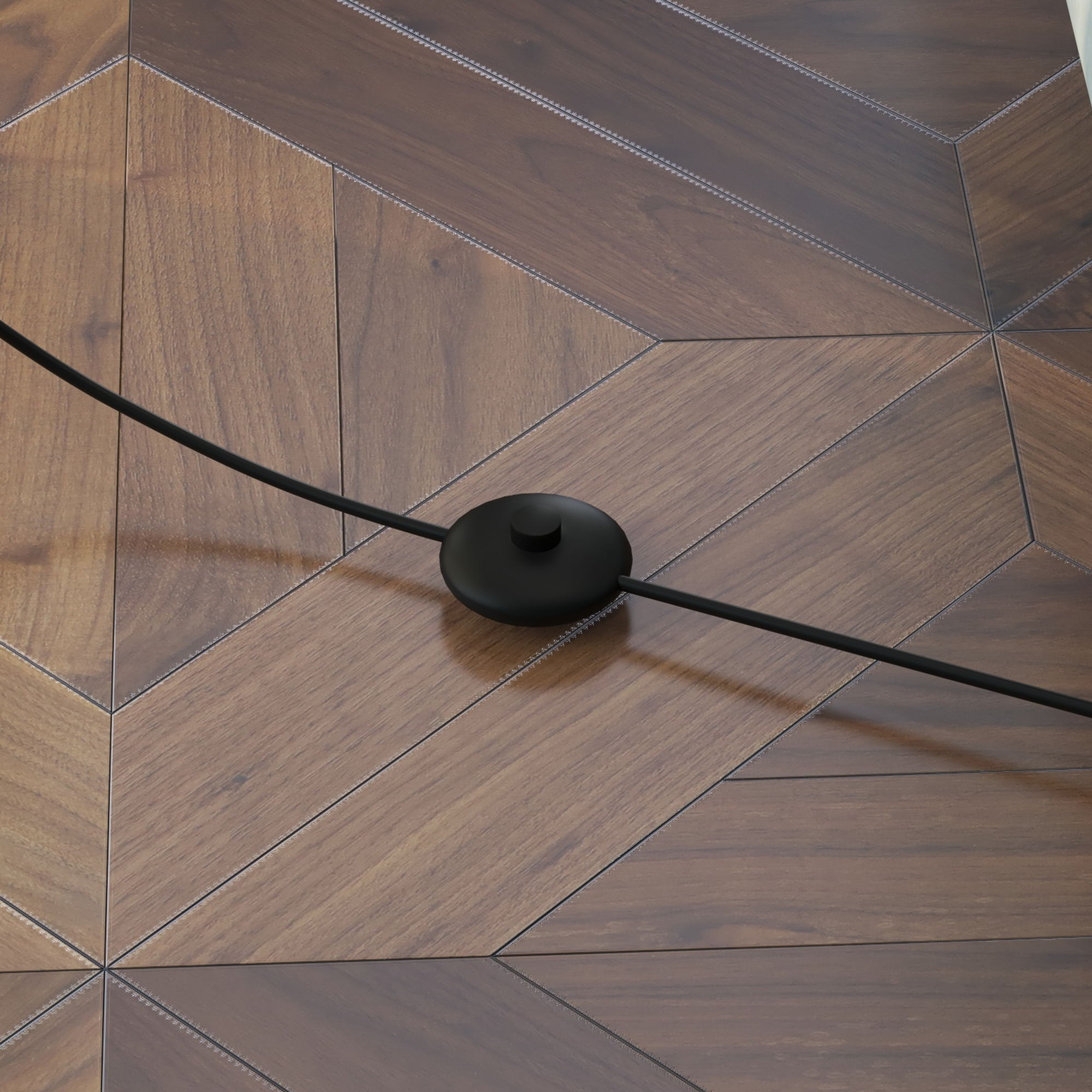 Primo piano di un pulsante di accensione nero e cavo su un pavimento in legno con motivo geometrico.