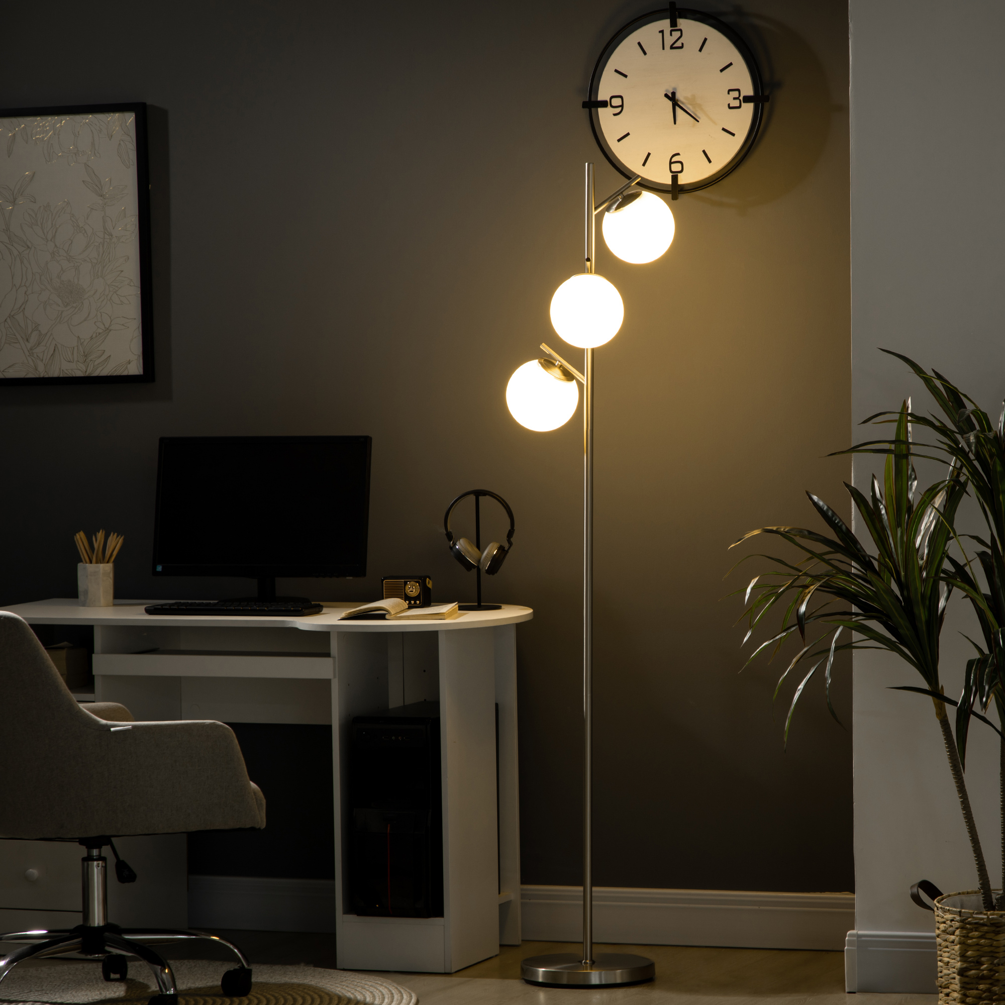 Lampada da terra con tre globi bianchi, accanto a scrivania, computer e orologio a muro.