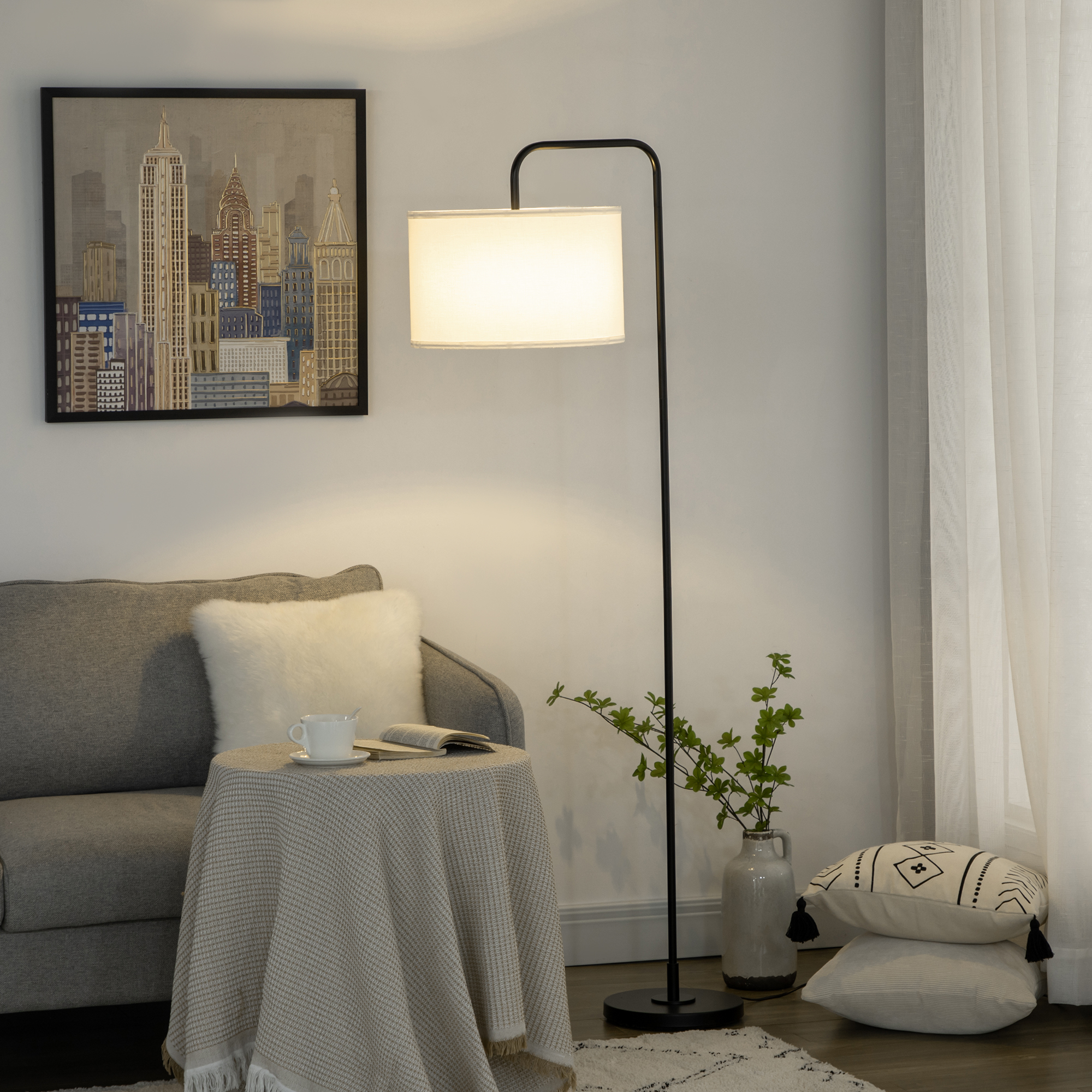 Una lampada da terra nera con un paralume bianco. Un divano, un tavolo e arte sullo sfondo.