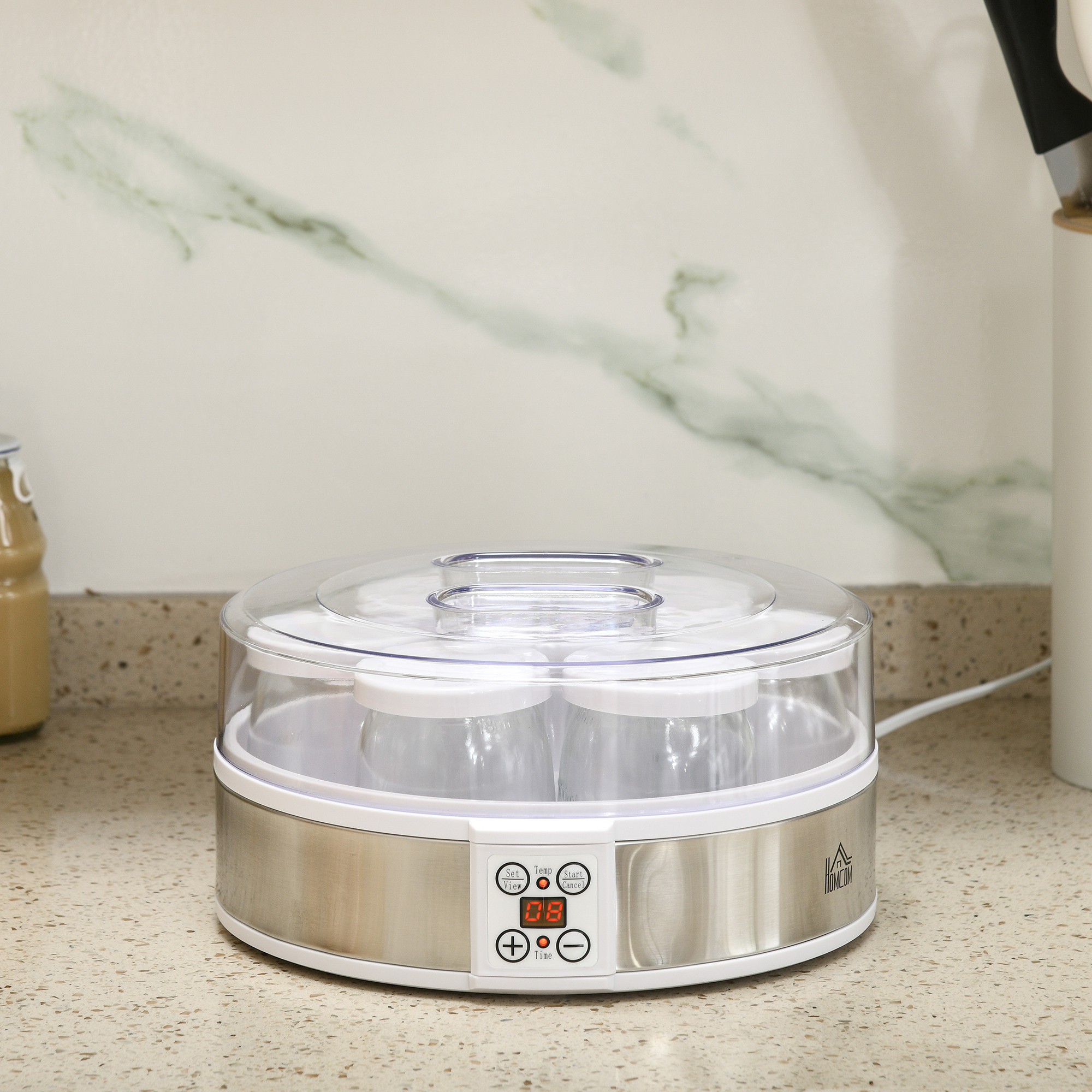 Yogurtiera con coperchio trasparente, pulsanti e display, su un piano cucina.
