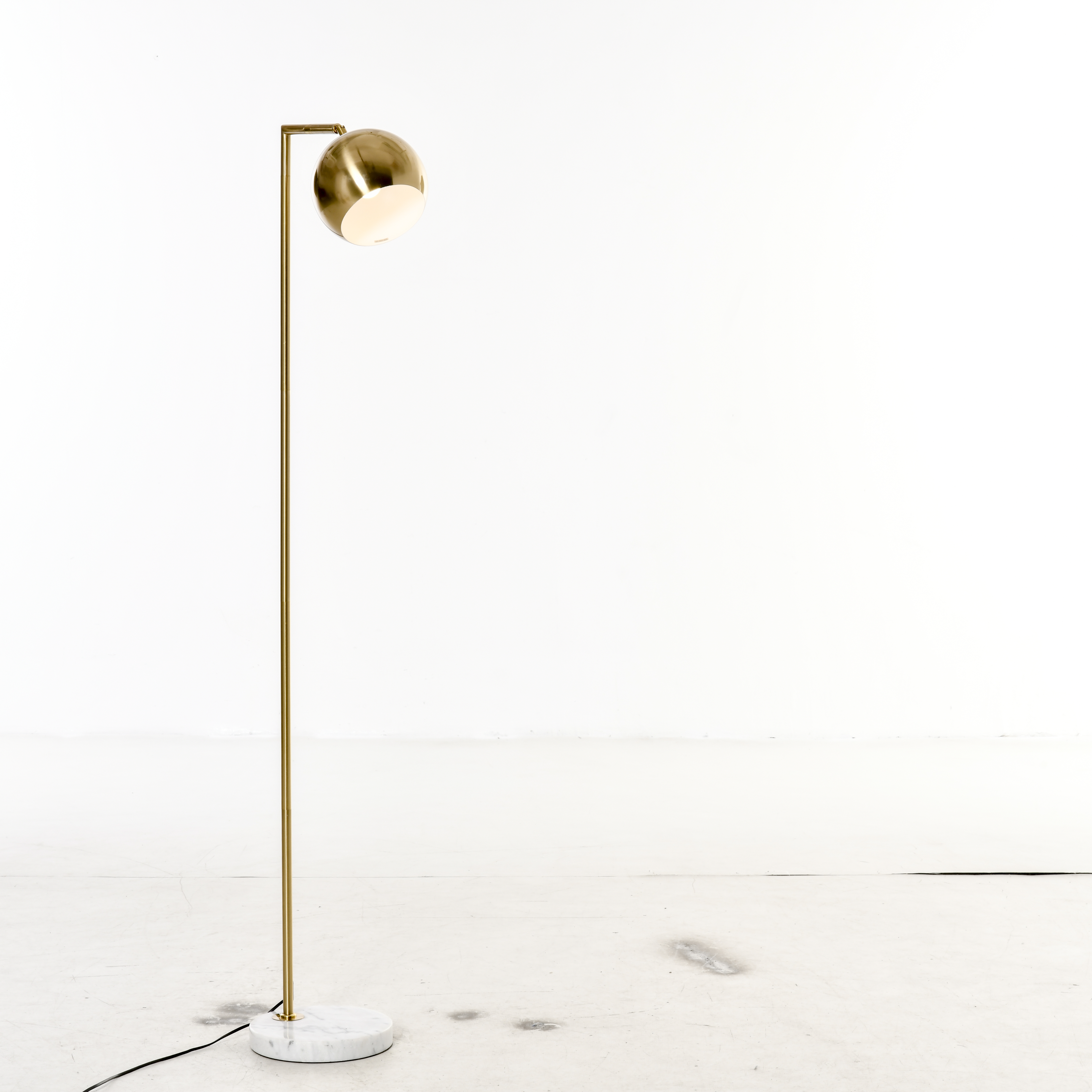 Una lampada da terra dorata con paralume sferico su sfondo bianco.