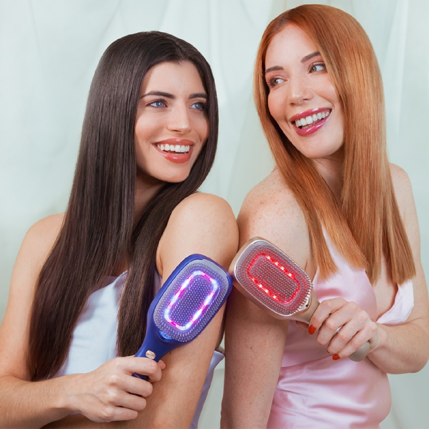 Due donne tengono spazzole per capelli con luci. Una ha i capelli scuri, l'altra rossi. Entrambe sorridono.