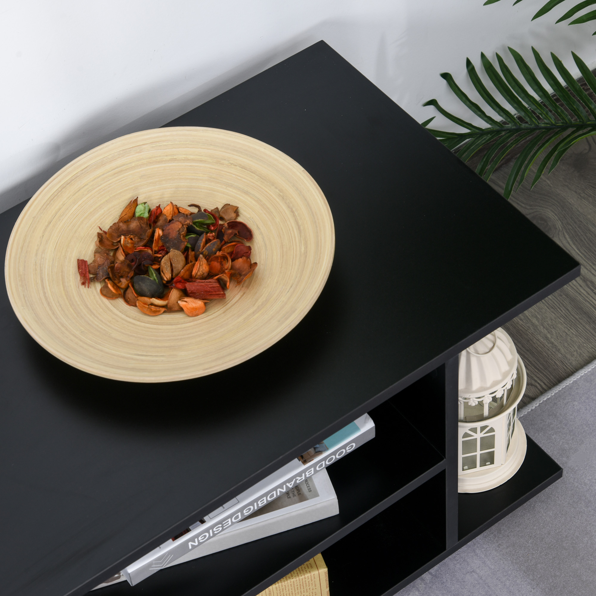 Un tavolino nero con una ciotola di legno. La ciotola contiene fiori secchi.