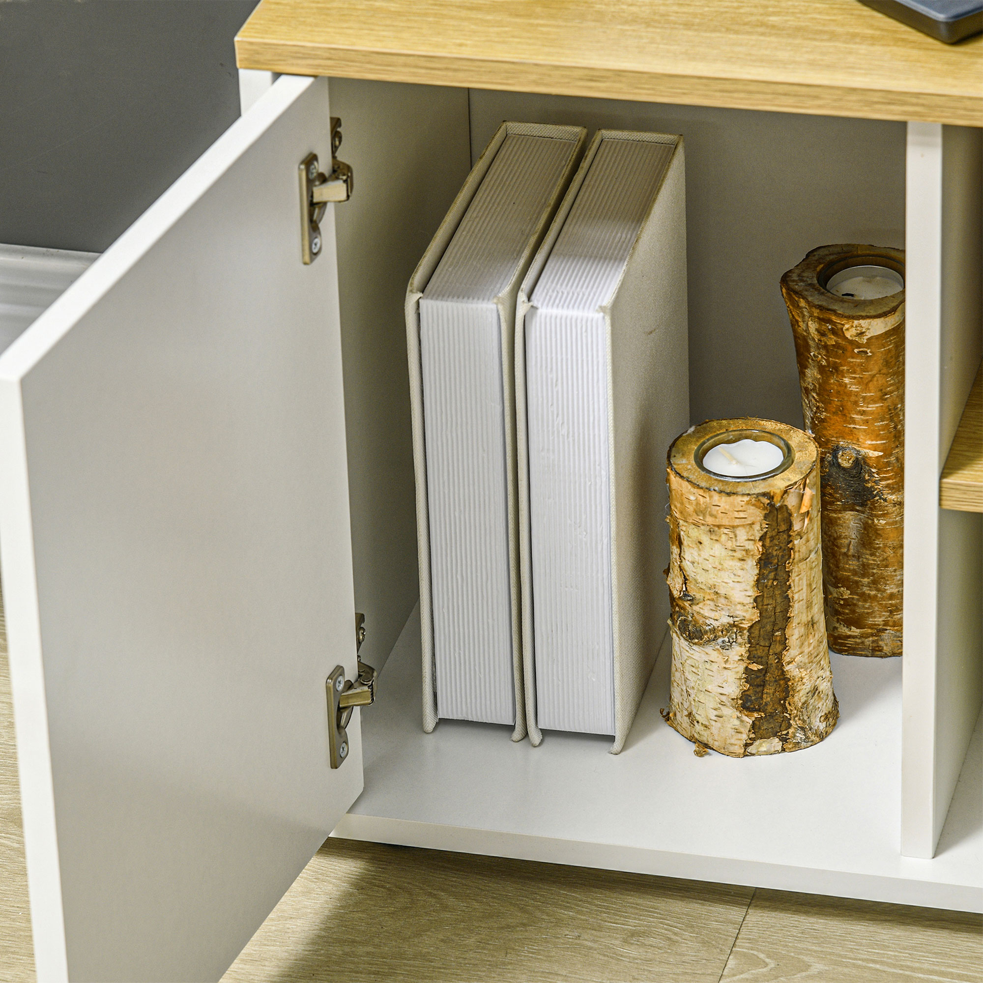 Armadio aperto con due libri e portacandele in betulla all'interno. Legno chiaro e armadio bianco con cerniere metalliche.