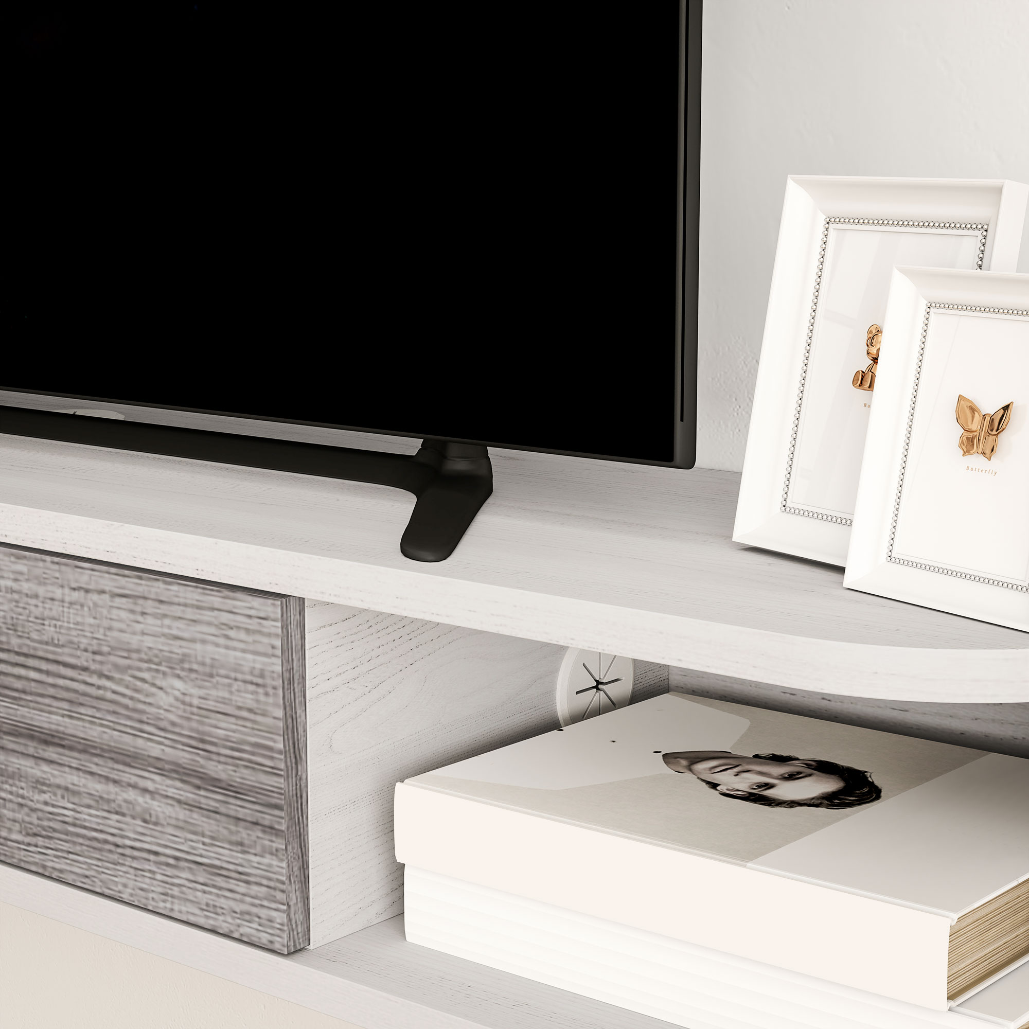 Primo piano di un mobile TV bianco con decorazioni. Sfondo: TV e foto incorniciate.