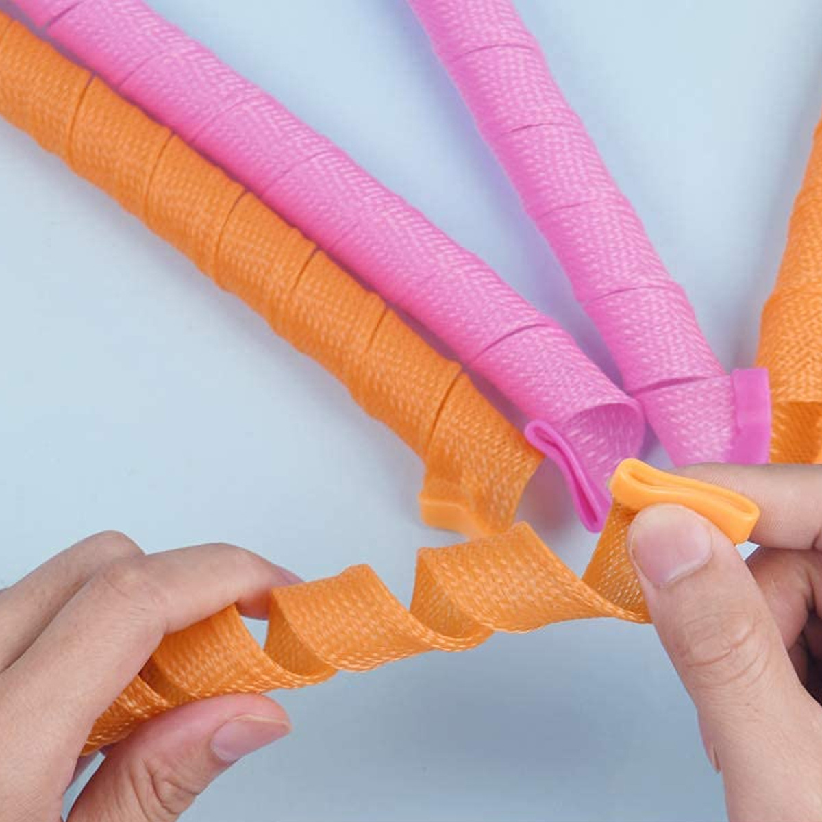 Hände halten orangefarbene und rosa Spiral-Haarroller. Der Lockenwickler wird abgewickelt, um das Netz zu zeigen.