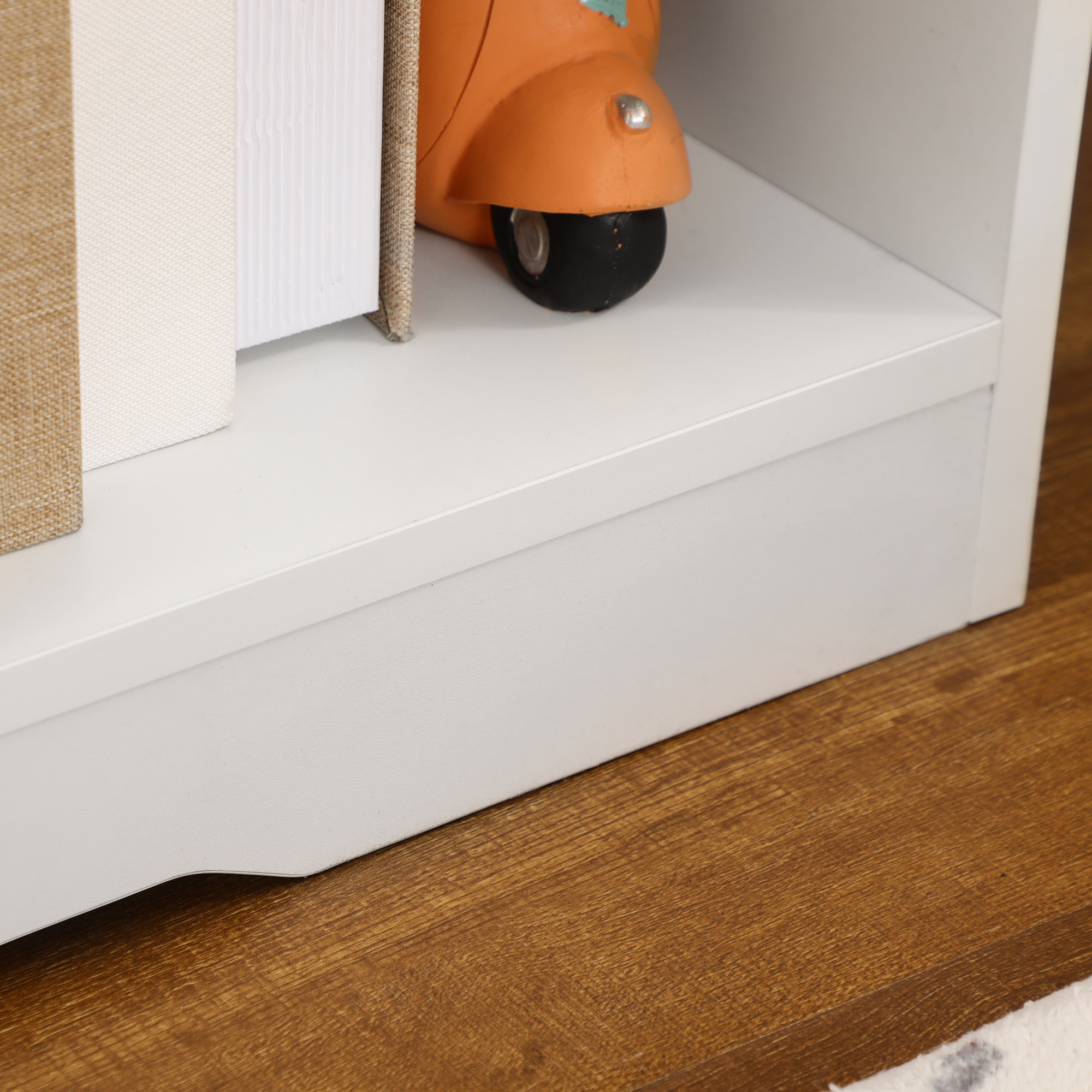 Primo piano di un ripiano bianco con oggetti decorativi: libri e uno scooter arancione.