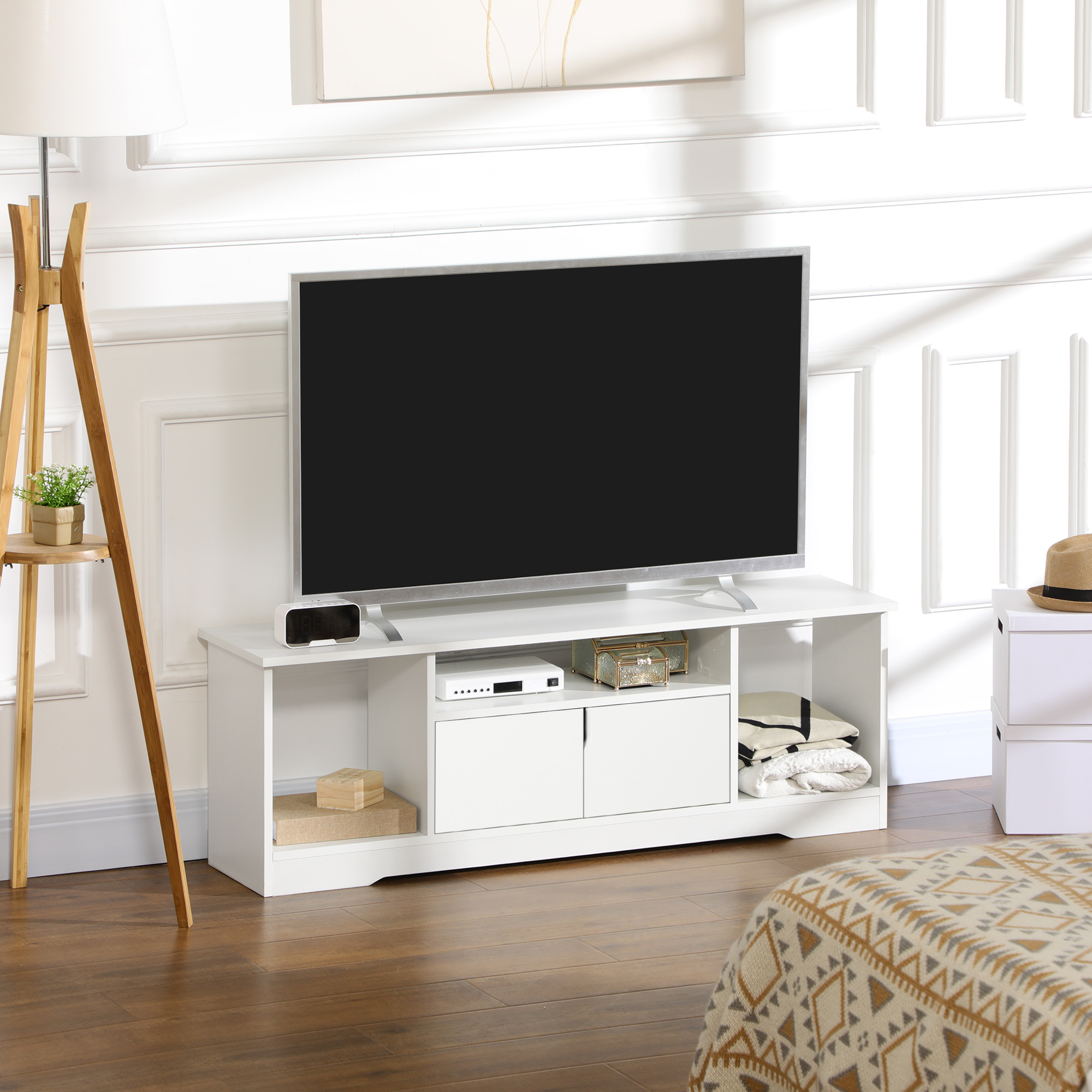 Mobile TV bianco con TV, altoparlanti e decorazioni, in una stanza con pavimento in legno.