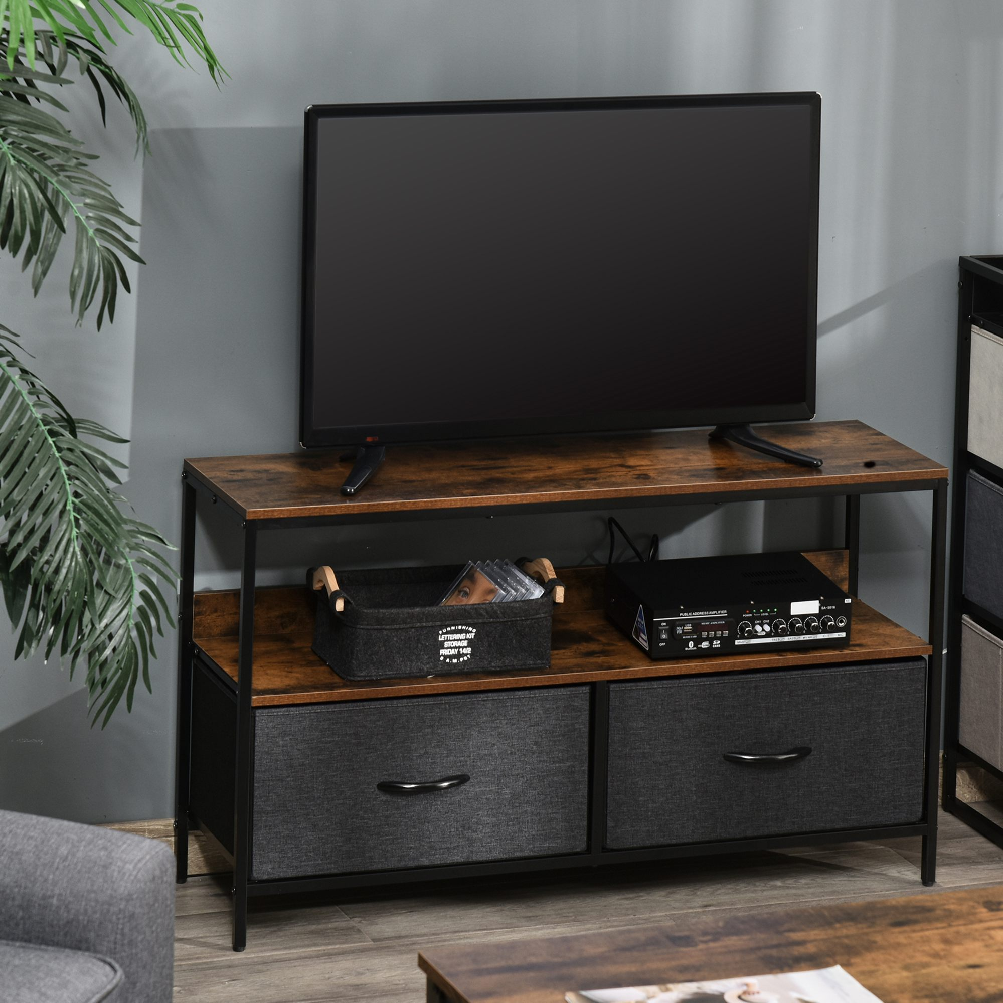 Un mobile TV marrone e nero con una TV sopra. Ha cassetti e ripiani. Lo sfondo è grigio.