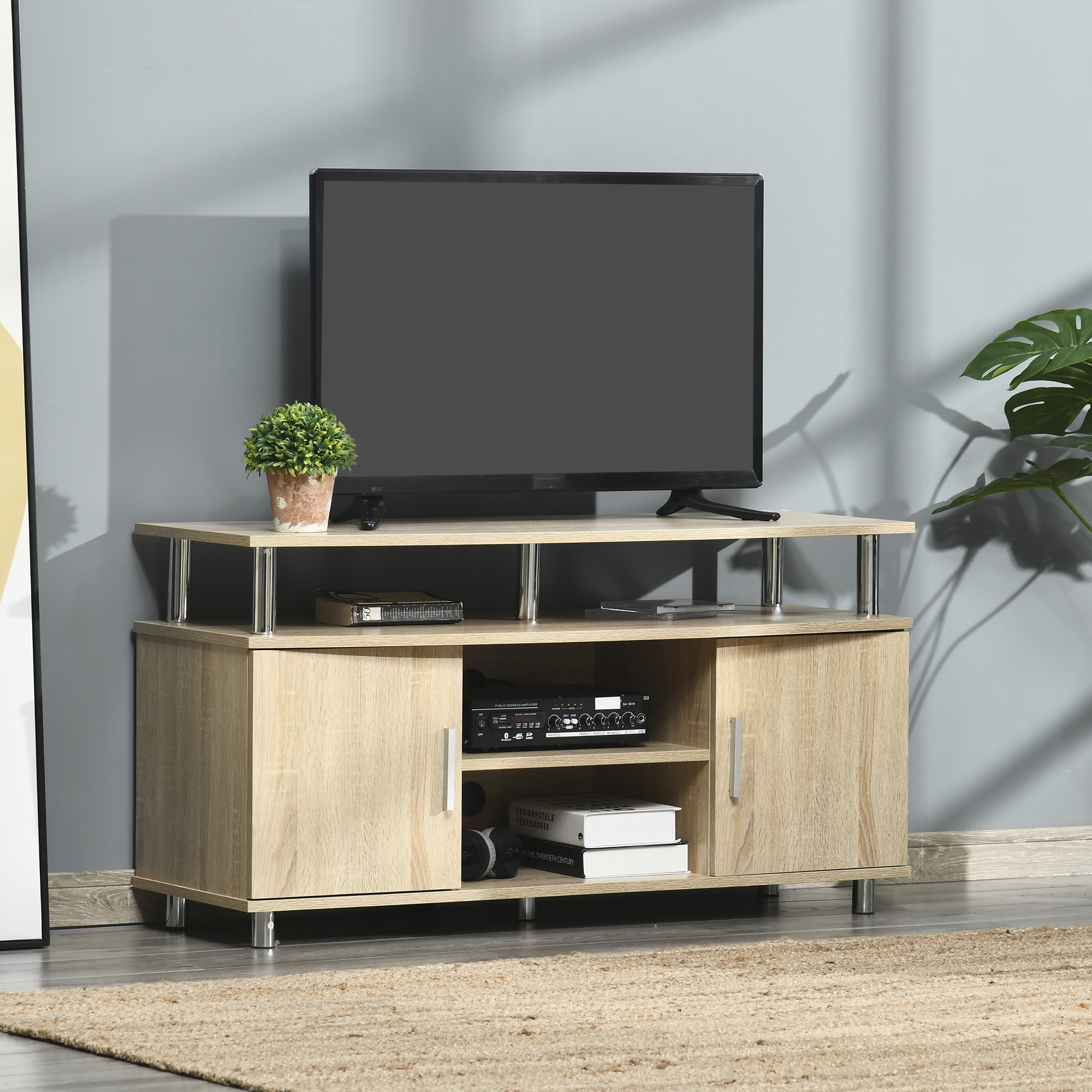 TV su un mobile TV colorato chiaro. Altoparlanti e decorazioni sono vicini. Una pianta è sul supporto.