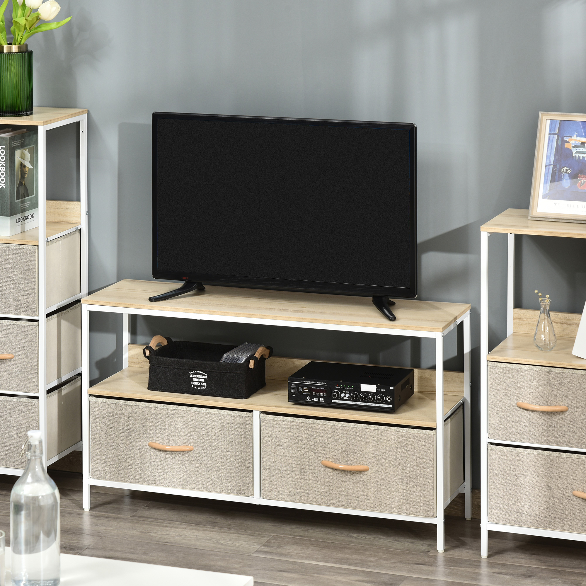 TV su un mobile TV in legno chiaro e bianco con cassetti. Altri mobili e un vaso ai lati.