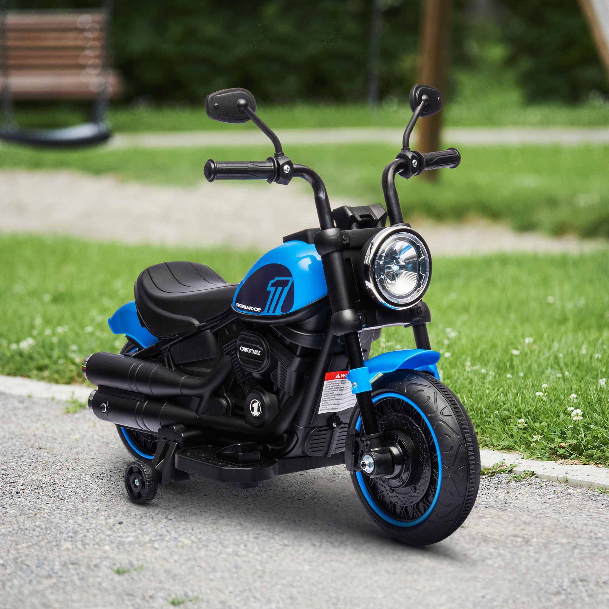 Moto giocattolo blu su un sentiero di ghiaia. La moto ha un faro e un corpo nero. Erba verde sullo sfondo.