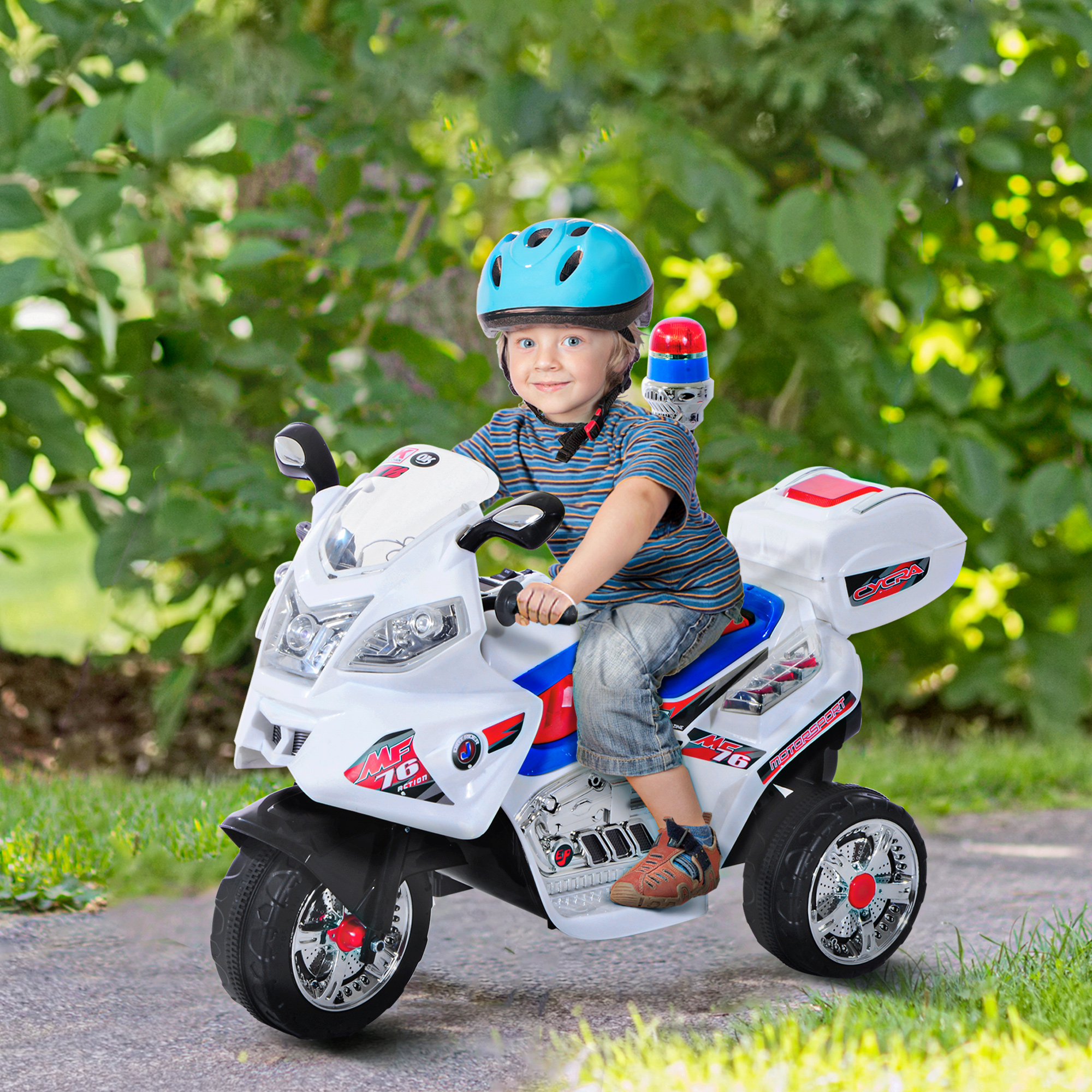 Un ragazzino con un casco blu guida una moto della polizia giocattolo bianca su un sentiero in un giardino verde.