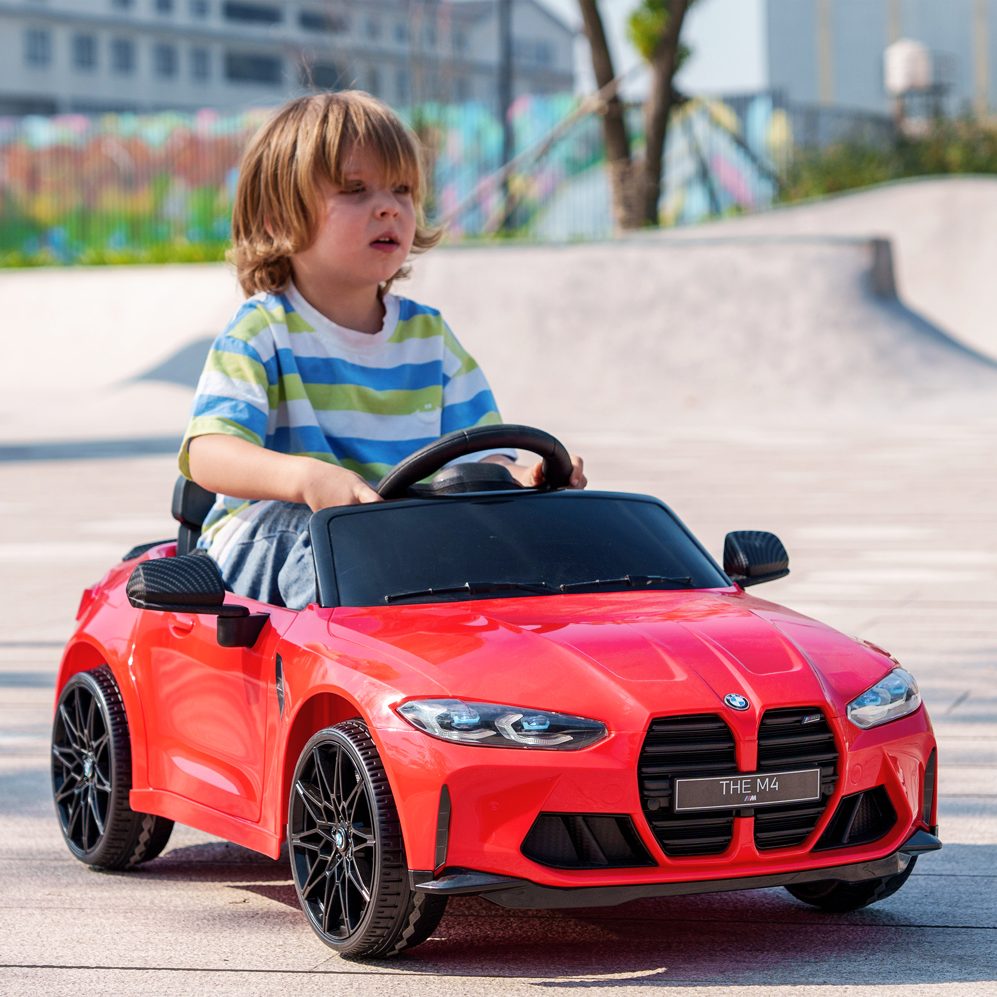 Un bambino guida un'auto giocattolo rossa. L'auto ha ruote nere. La scena si svolge all'aperto.