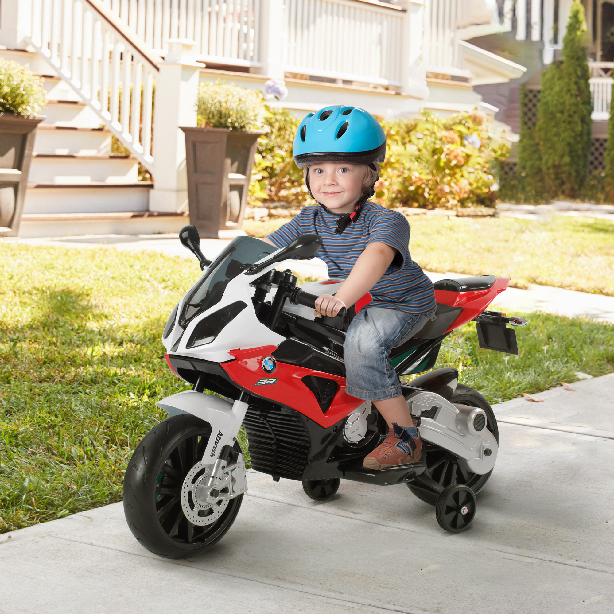 Un bambino su una moto giocattolo rossa e bianca con un casco. La scena è all'aperto, davanti a una casa.