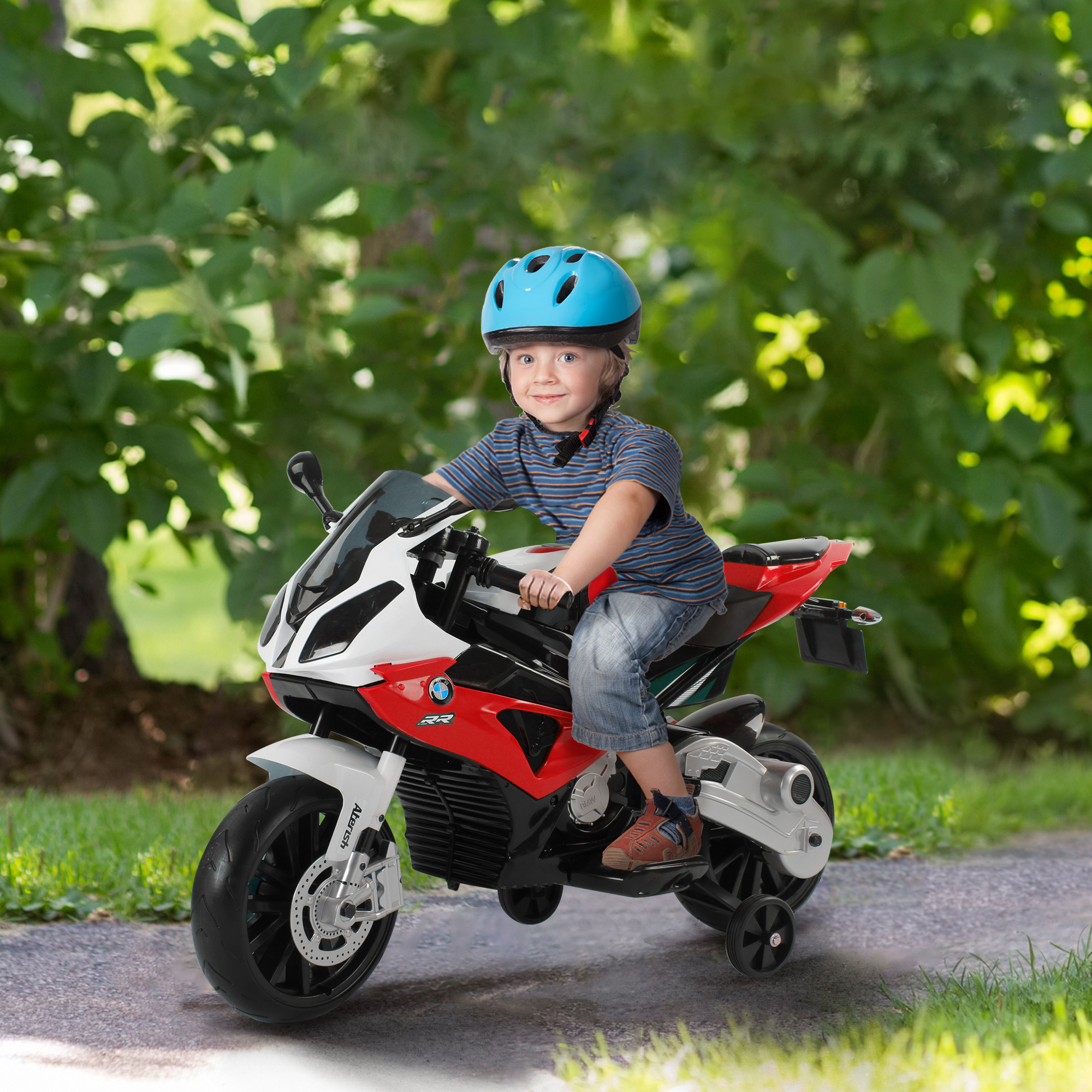 Un ragazzino con un casco guida una moto giocattolo su un sentiero. Alberi verdi sullo sfondo.