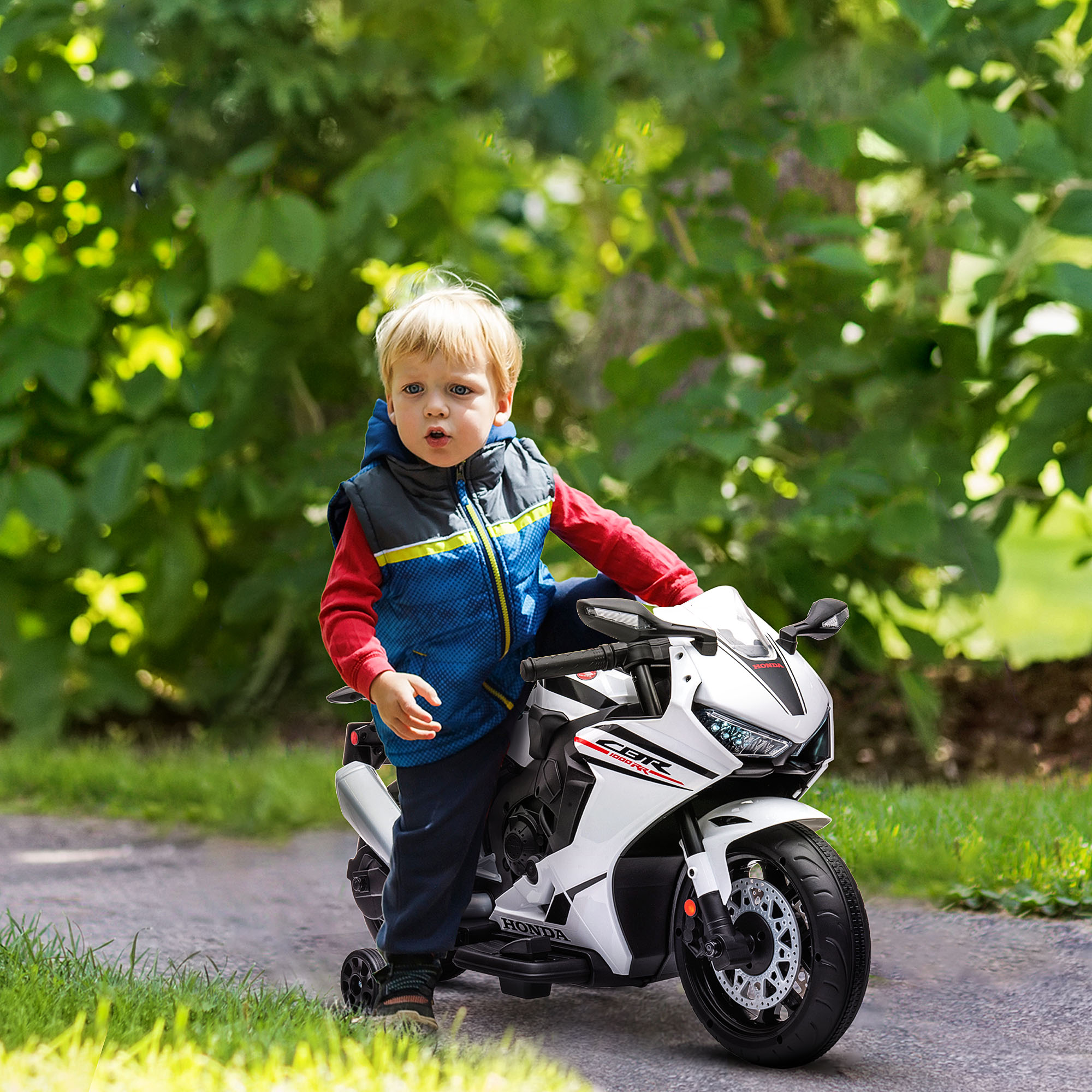 Un bambino su una moto giocattolo bianca e nera. Indossa una giacca blu e guarda la fotocamera.