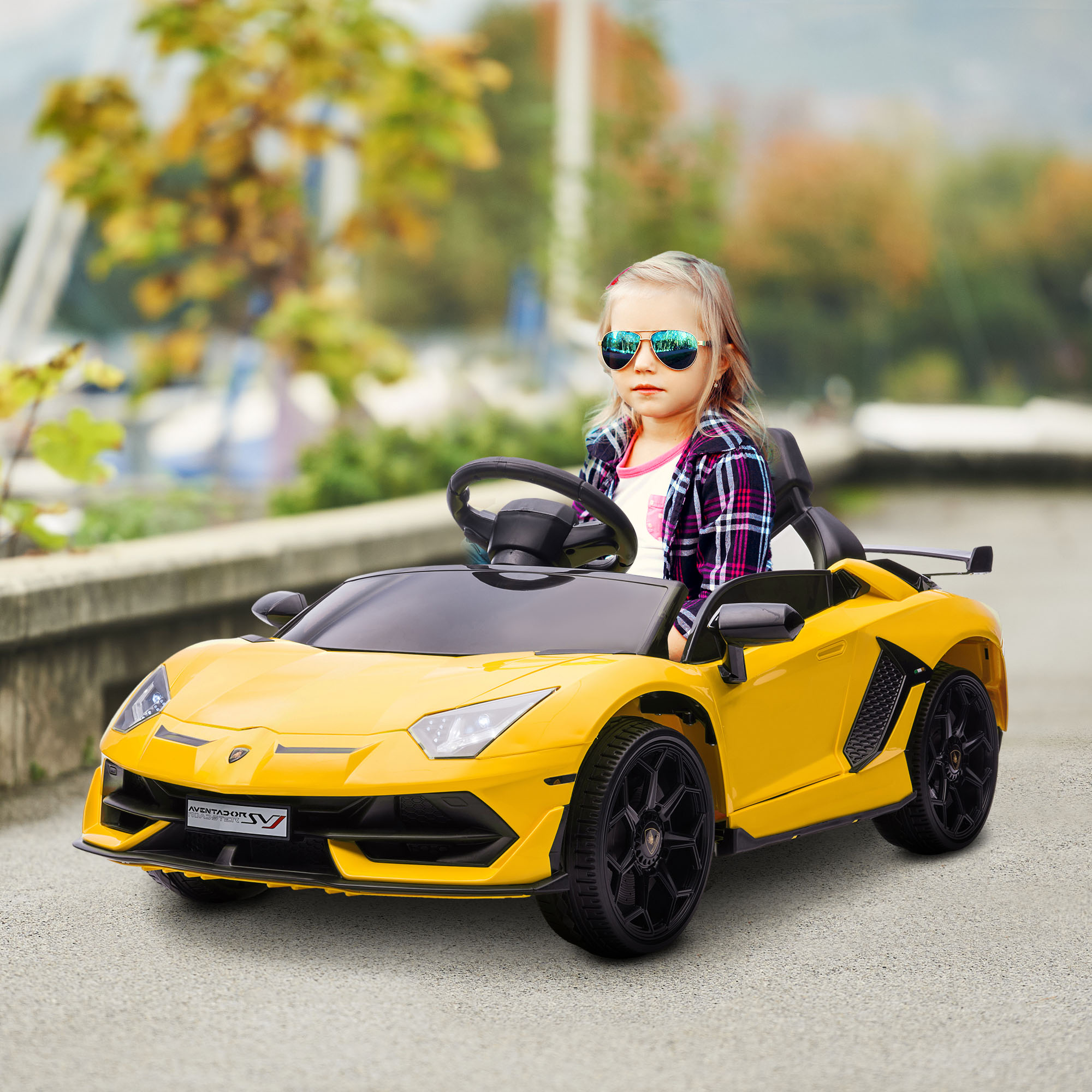 Auto giocattolo Lamborghini gialla con un bambino con occhiali da sole alla guida. Sfondo: alberi e strada.
