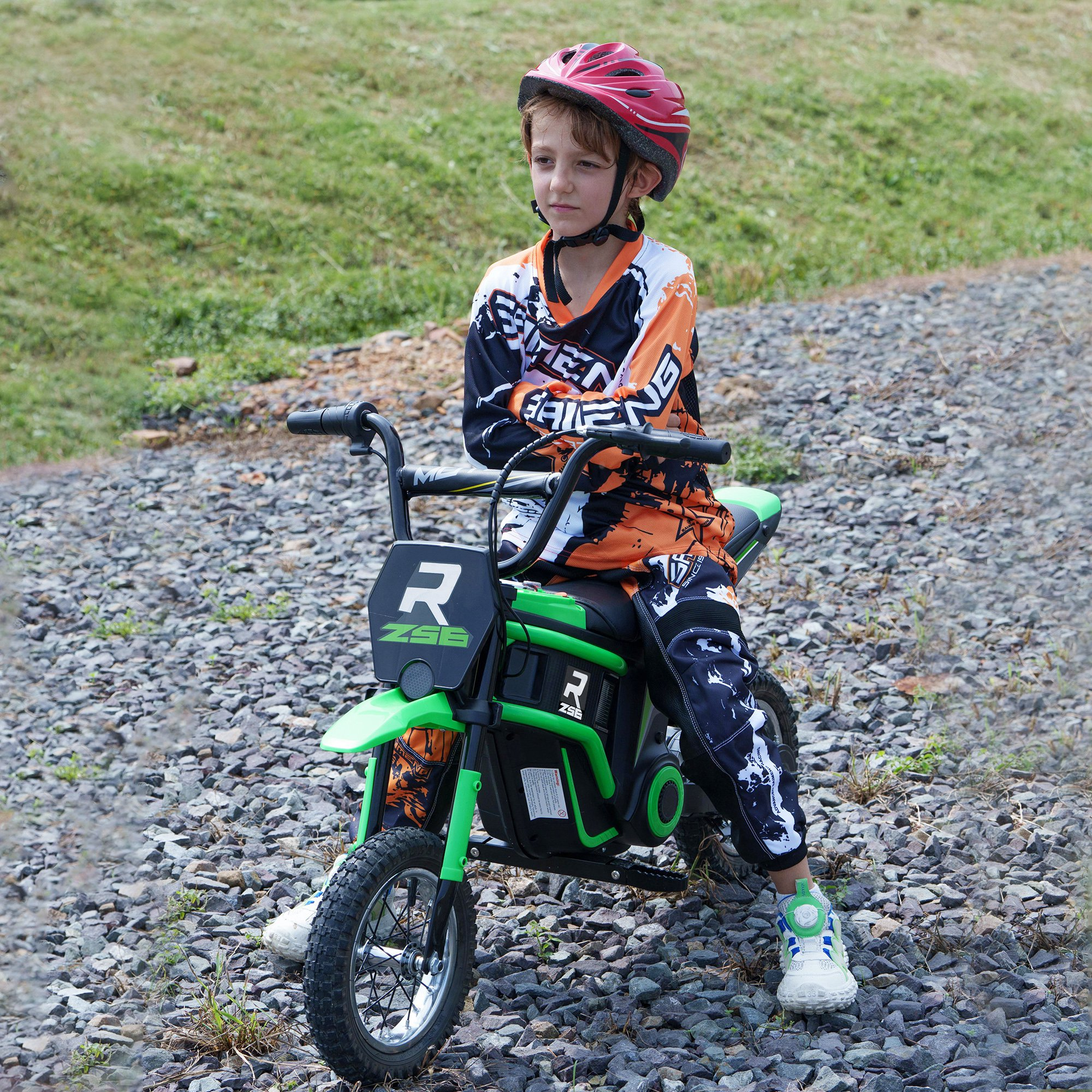 Un bambino su una moto giocattolo verde con casco, in tuta da corsa, su un sentiero roccioso.