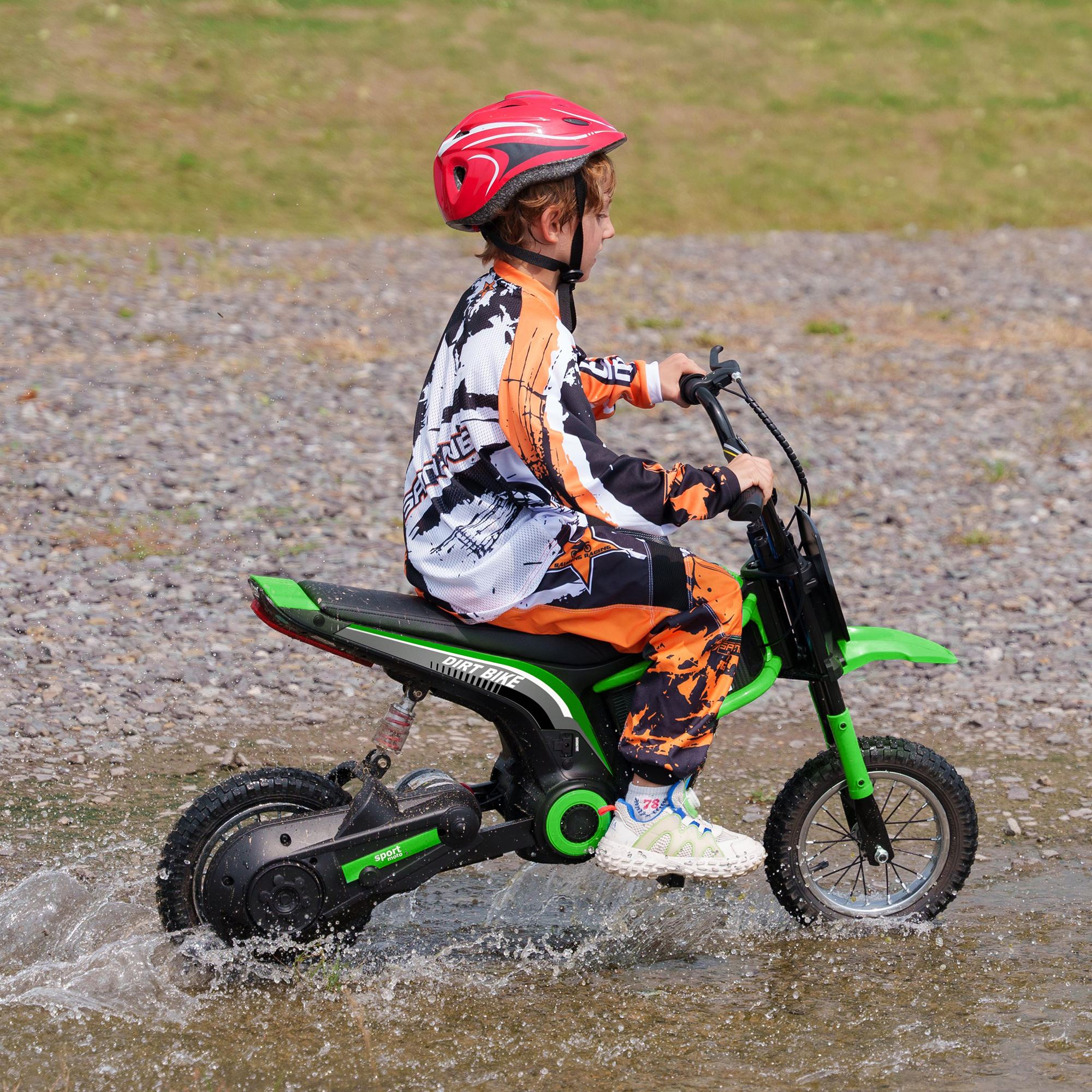 Un bambino in tenuta da corsa guida una moto giocattolo verde e nera nell'acqua. Casco rosso.