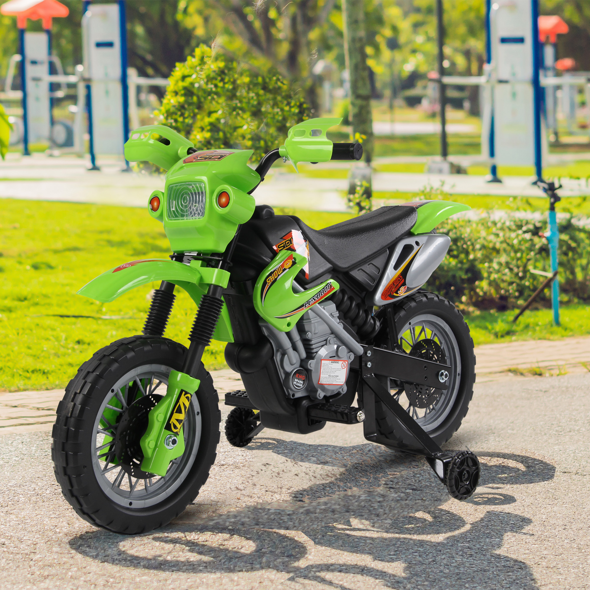 Una moto giocattolo verde con rotelle, parcheggiata su una superficie pavimentata, vicino l'erba.