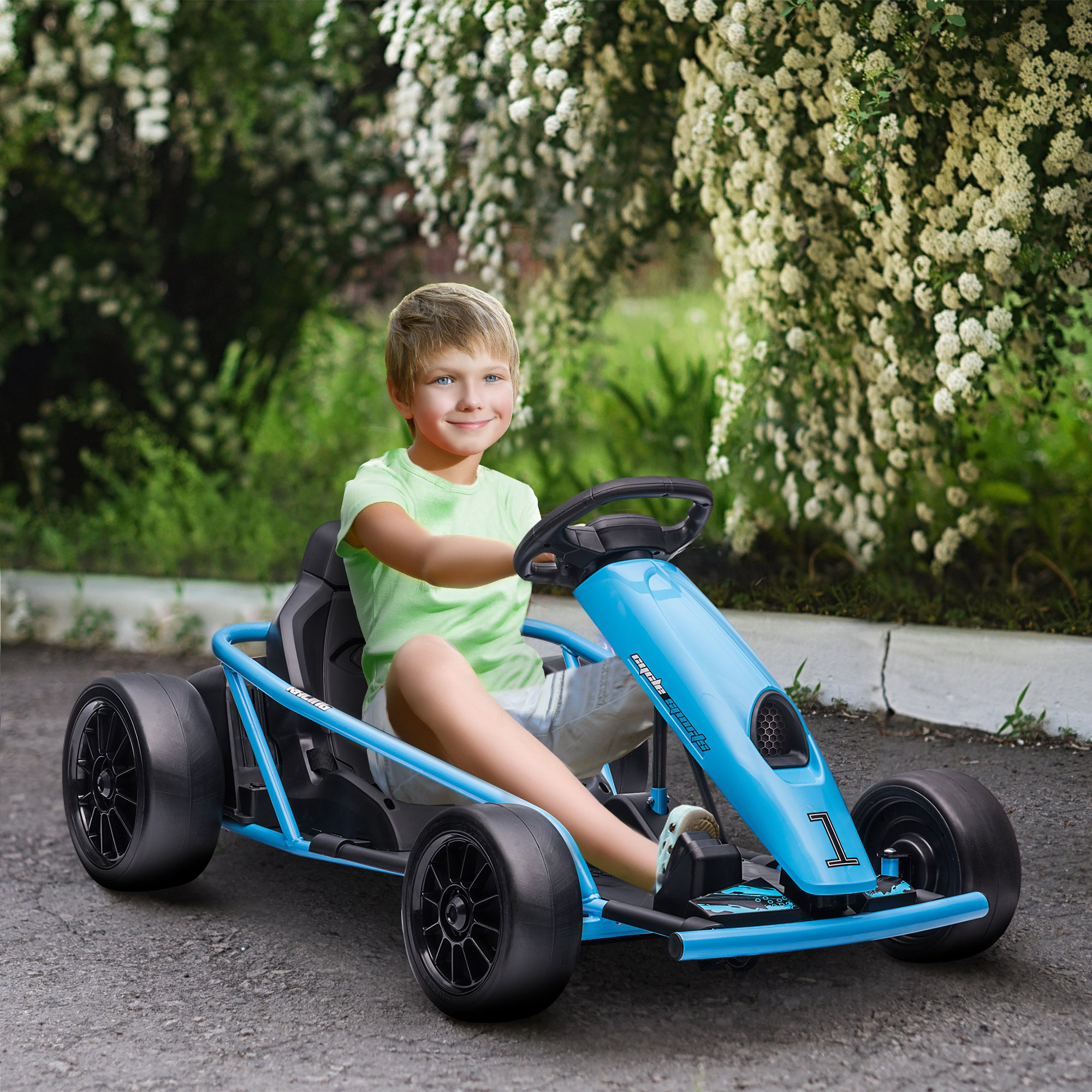 Un ragazzo guida un go-kart blu. Sorride. Fiori bianchi e cespugli verdi sullo sfondo.