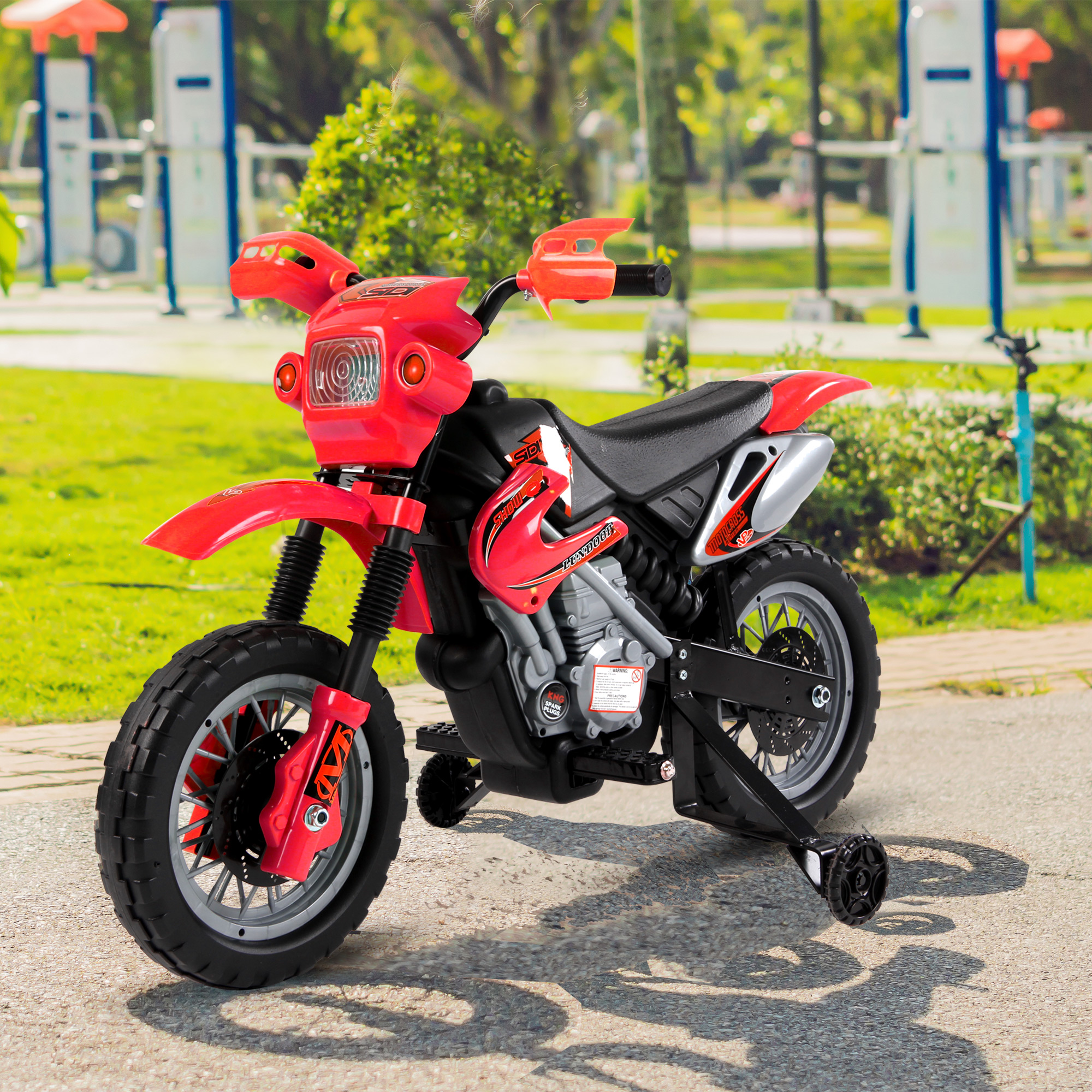 Una moto giocattolo rossa con rotelle su una superficie pavimentata, con sfondo di erba verde.