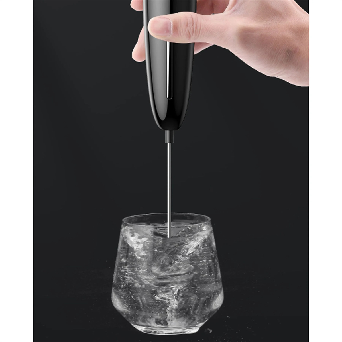 Eine Hand hält einen schwarzen Milchaufschäumer, der Milch in einem Glas Wasser aufschäumt. Dunkler Hintergrund.