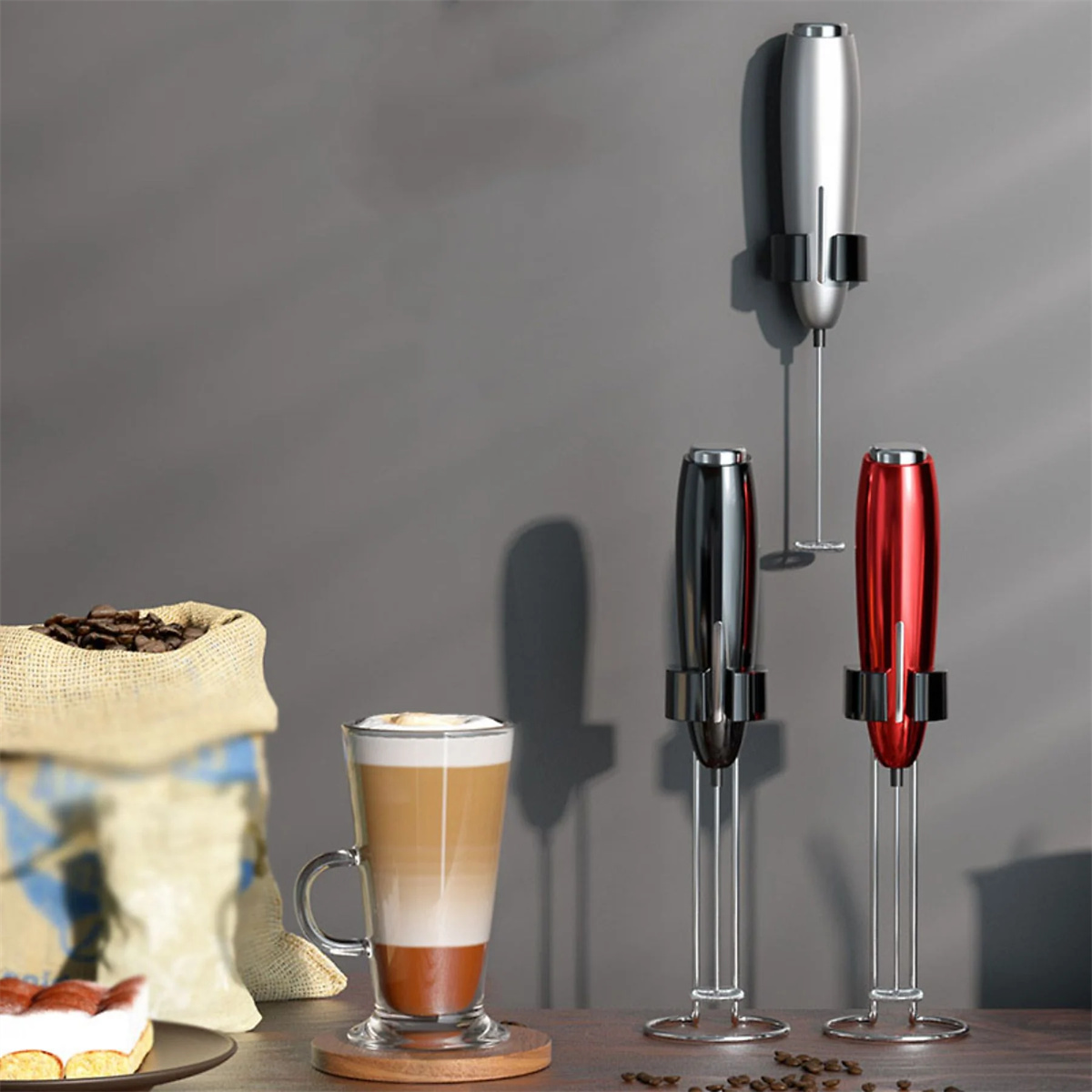 Drei Aufschäumer auf Ständern und ein Glas Latte mit Kaffeebohnen im Sack.
