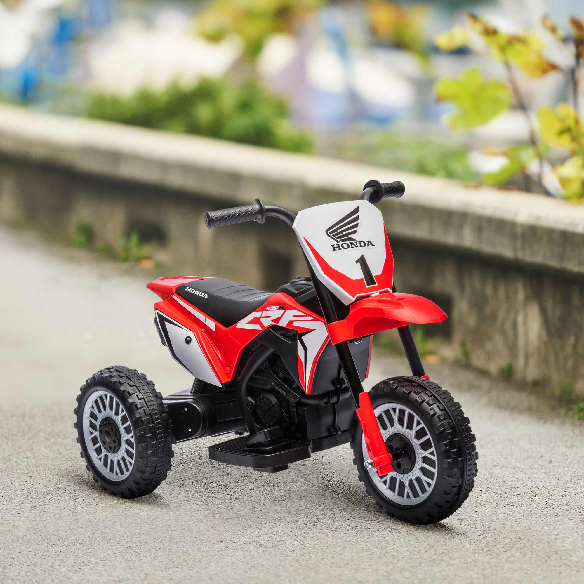 Moto Honda giocattolo rossa su una superficie pavimentata. La moto ha tre ruote e il numero 1 davanti.