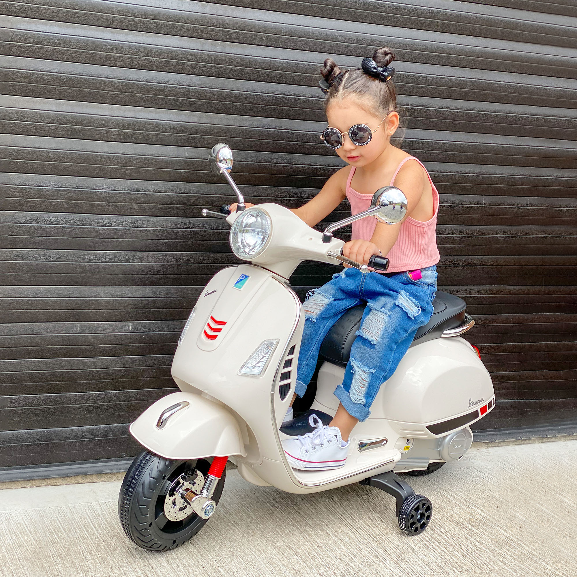 Un bambino su uno scooter giocattolo rosa. Sedile e dettagli neri. Bambino con occhiali da sole e jeans.
