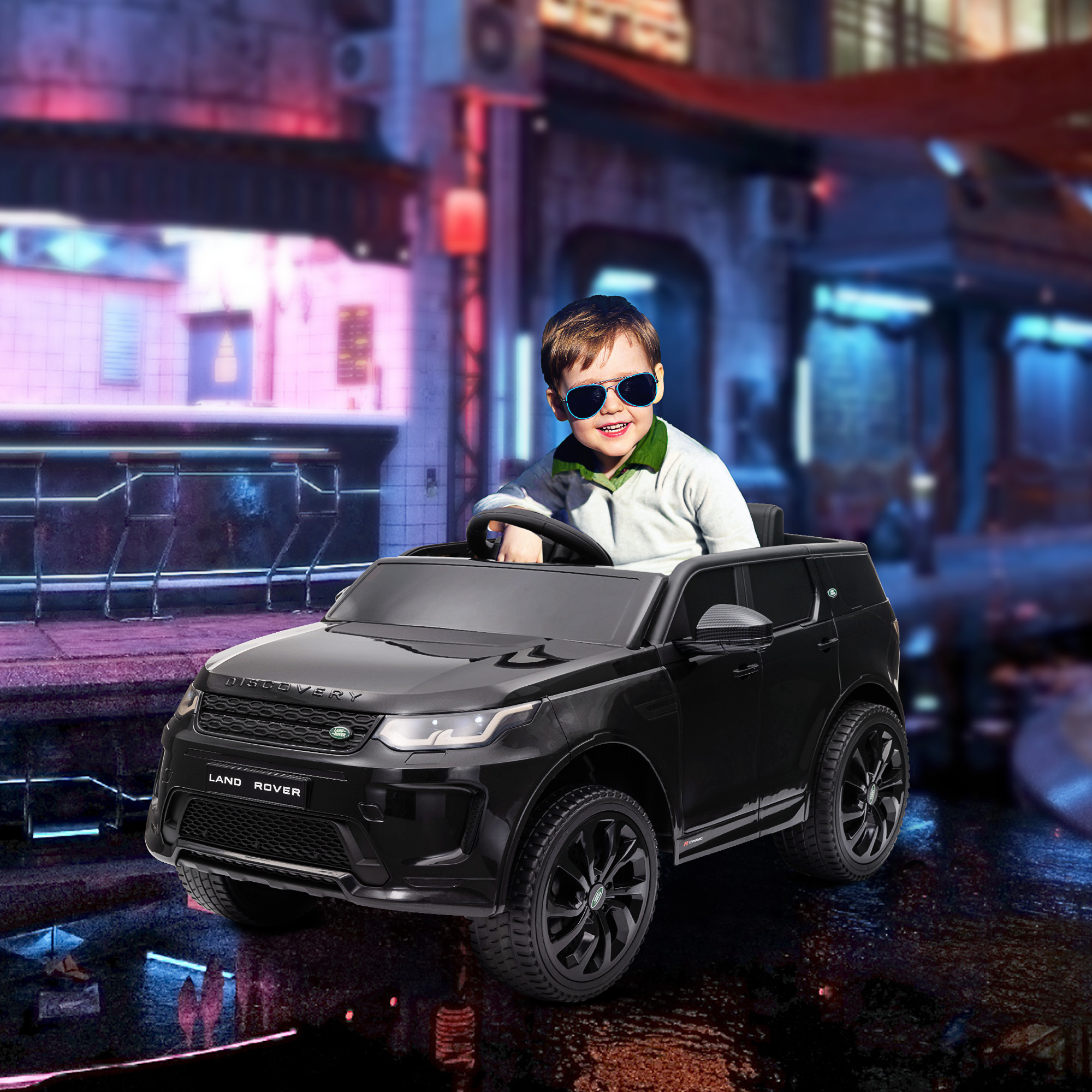 Ragazzo con occhiali da sole guida un Land Rover giocattolo nero in una scena cittadina.